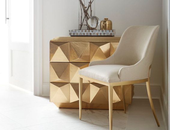 A chair is sitting next to a gold dresser in a room.