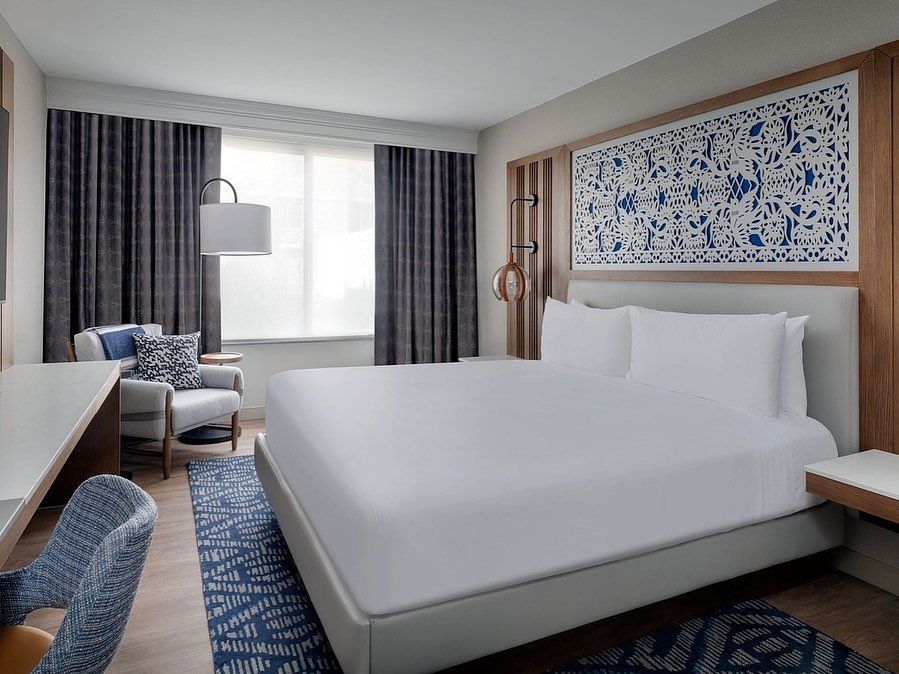 A hotel room with a king size bed , chair , desk and window.