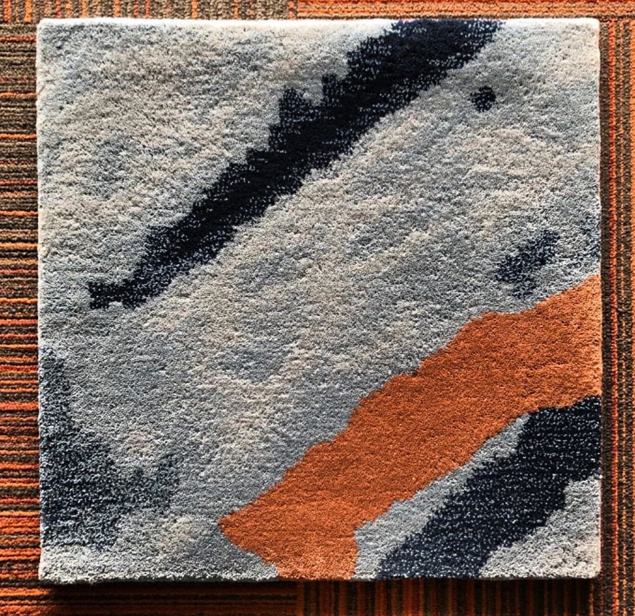 A square rug with a blue and orange pattern is sitting on a wooden table.