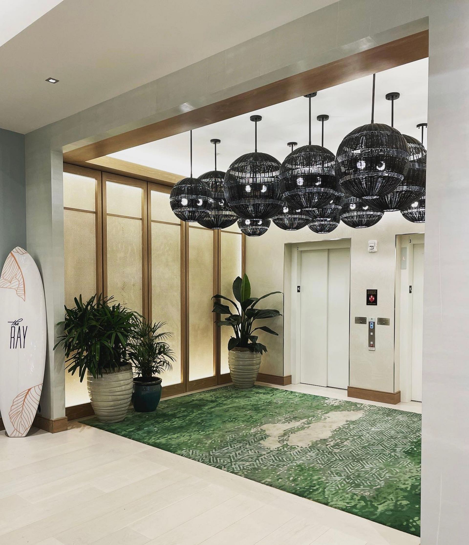 A hallway with a surfboard in the corner and a row of lamps hanging from the ceiling.