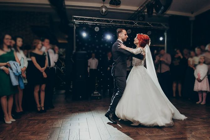 Bride and groom dancing in a dimly lit reception hall, guests watching nearby
