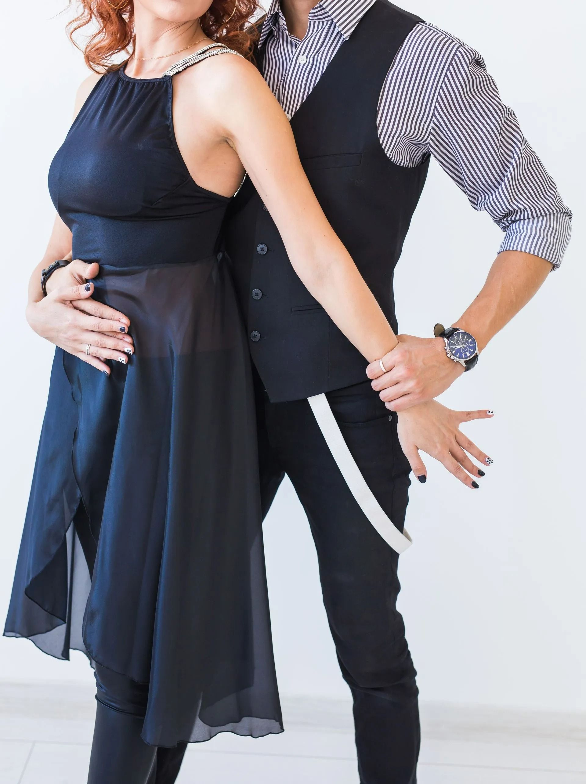 Couple posing in formal black outfits, standing close together against a light background.