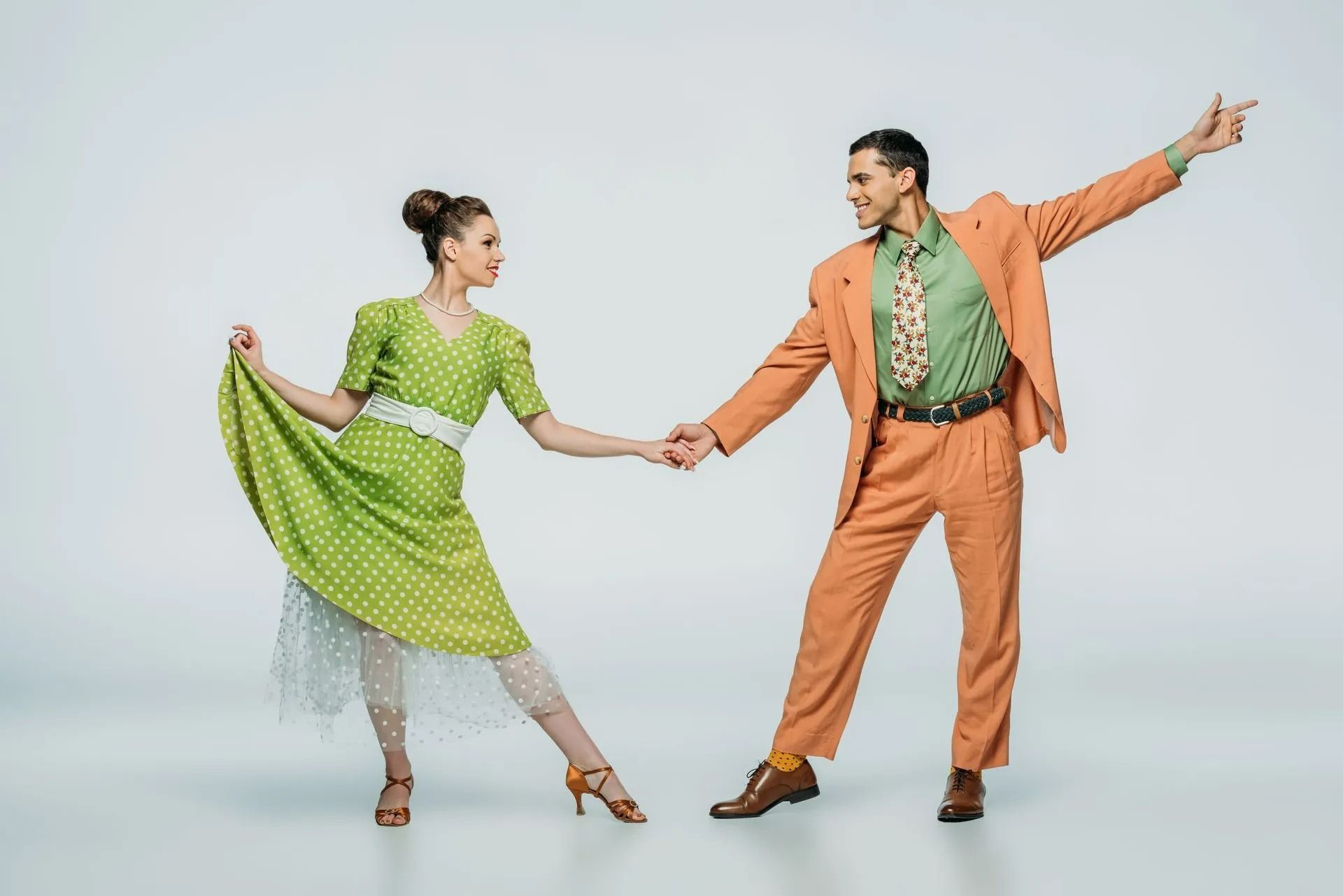 Two dancers in bright green and orange outfits holding hands against a plain light background