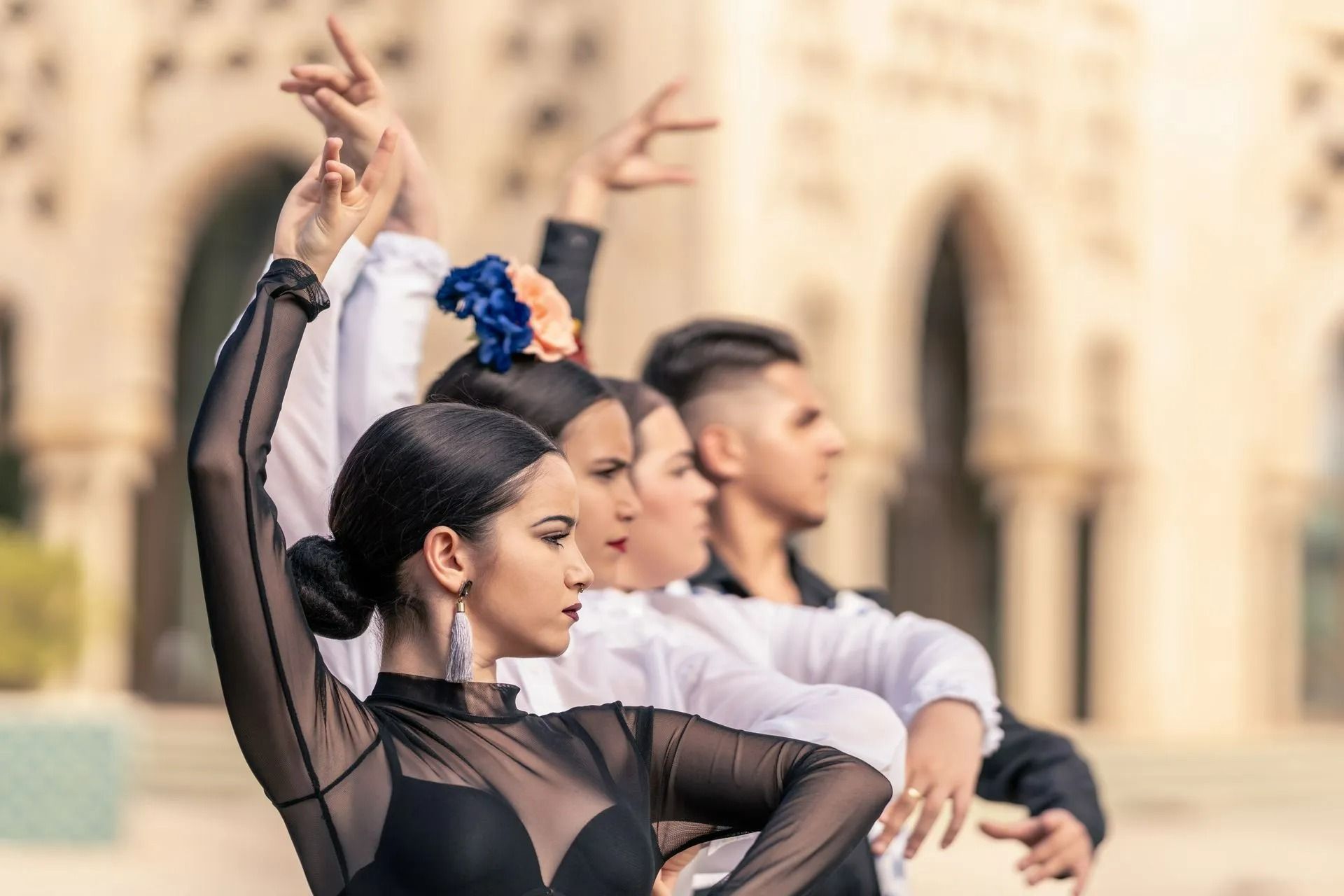 Dancers in black and white costumes performing synchronized arm movements outdoors before a stone building