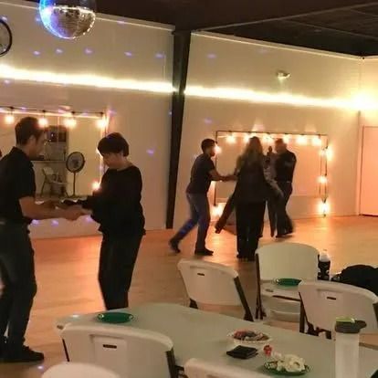 People dancing in a warmly lit hall with string lights and chairs in the foreground