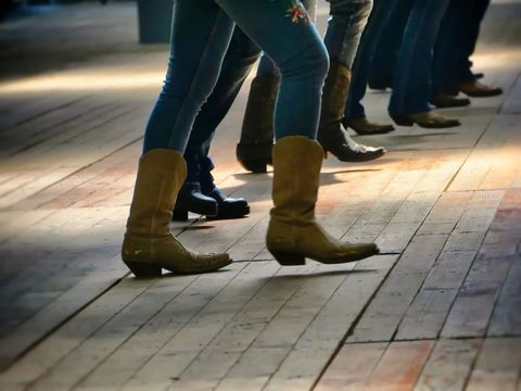 People standing in line on a wooden sidewalk, with one pair of tan boots in the foreground.
