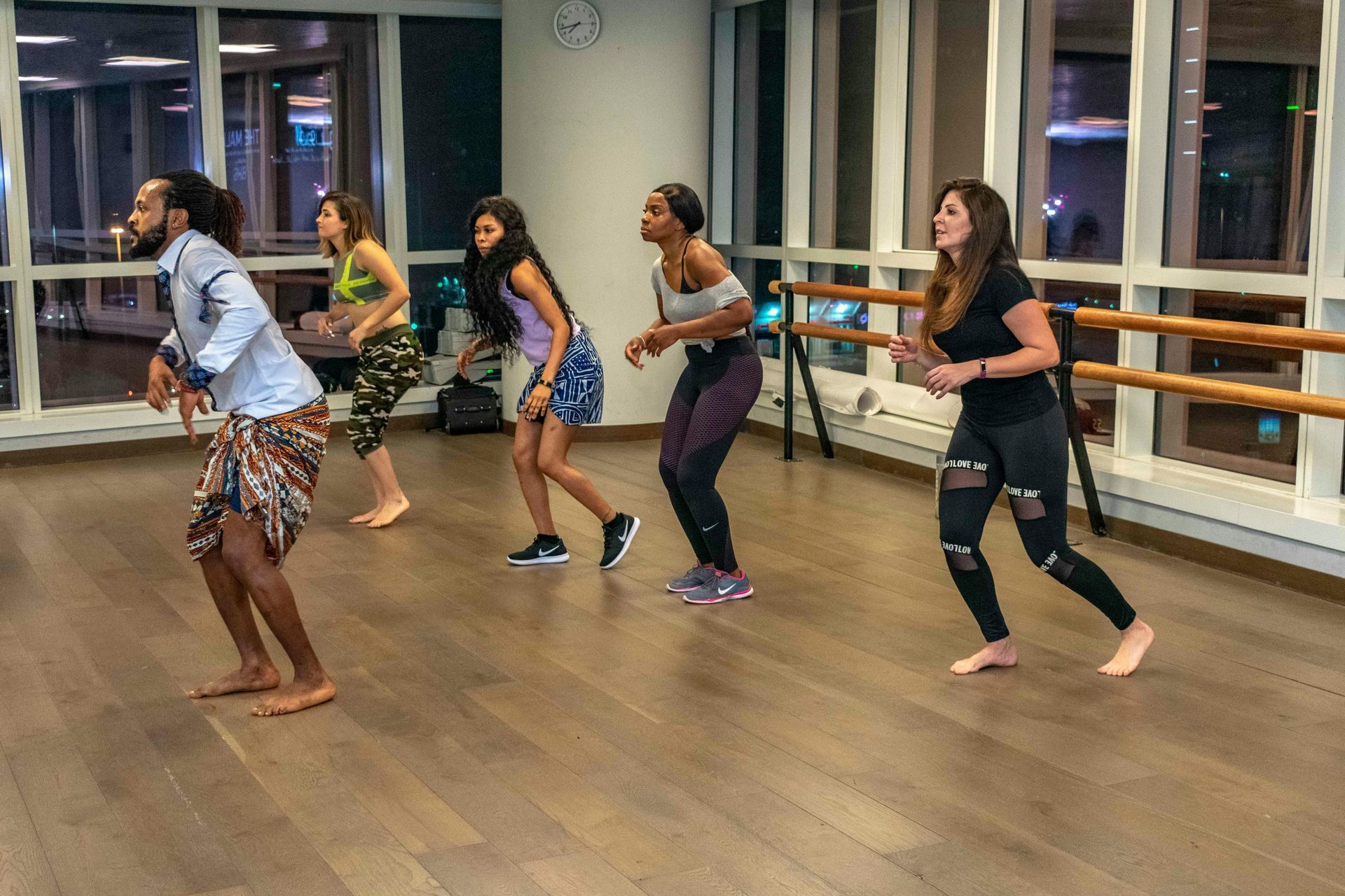 Five people dancing in a mirrored studio with wooden floors and large windows