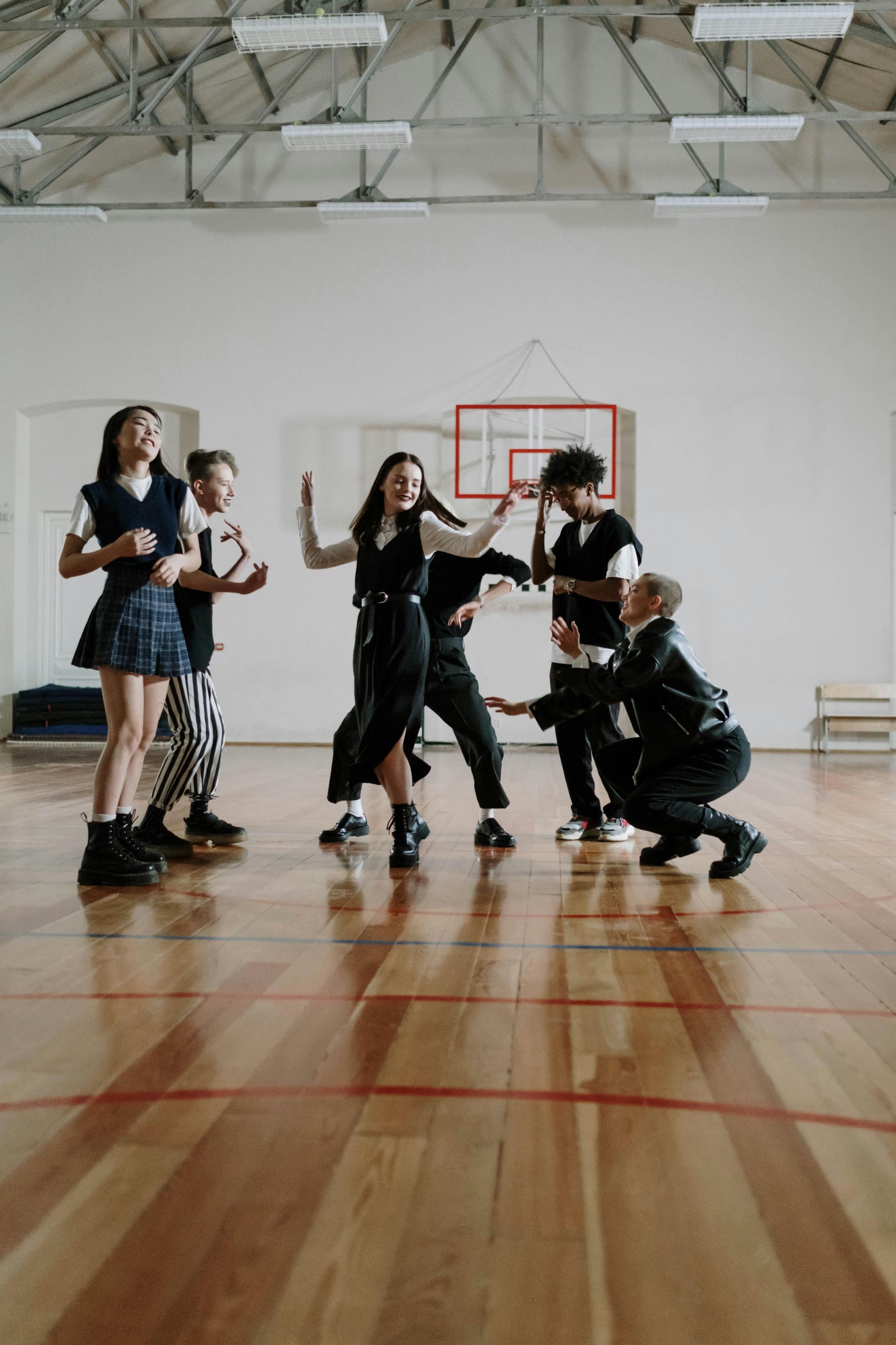 Group of people rehearsing a dance routine in a bright gym with a wooden floor and basketball hoop.