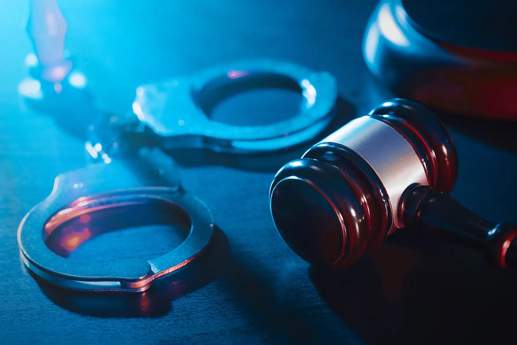 A pair of handcuffs and a judge 's gavel on a table, representing the topic of criminal defense law.
