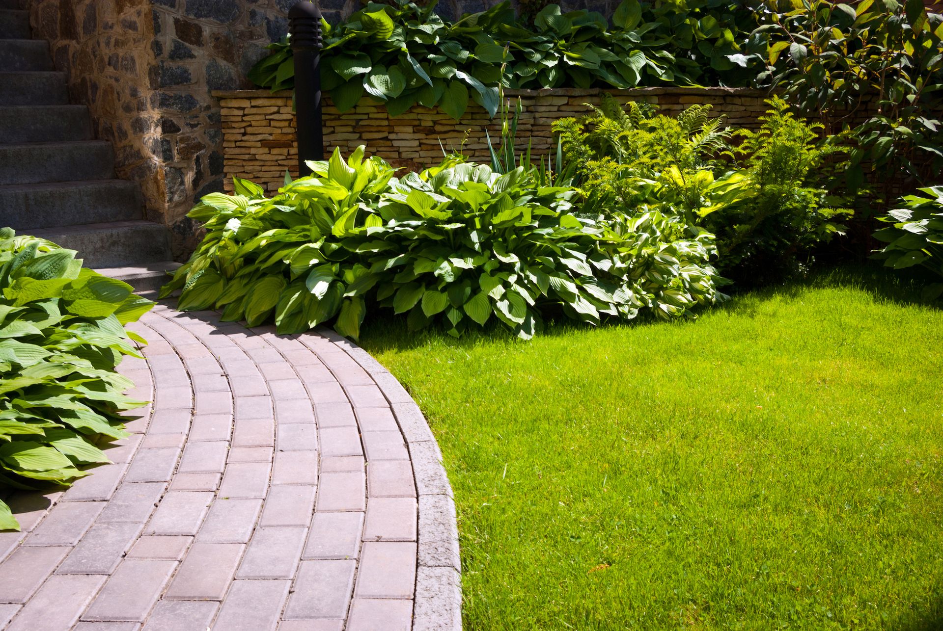 A brick walkway leading to a house with a lush green lawn.