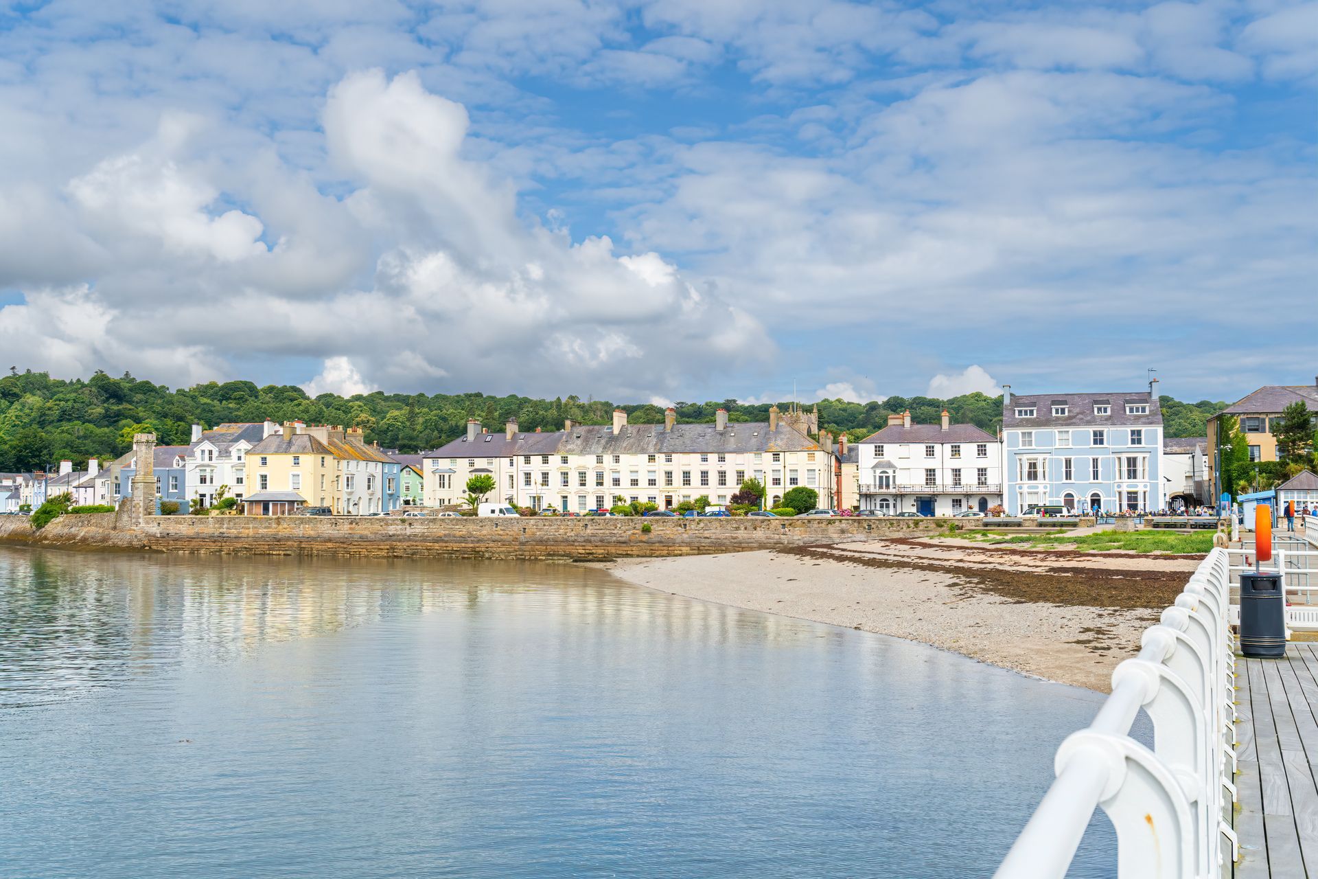 Colorful seaside cottages in Beaumaris with a sandy beach beside calm sea under a cloudy sky