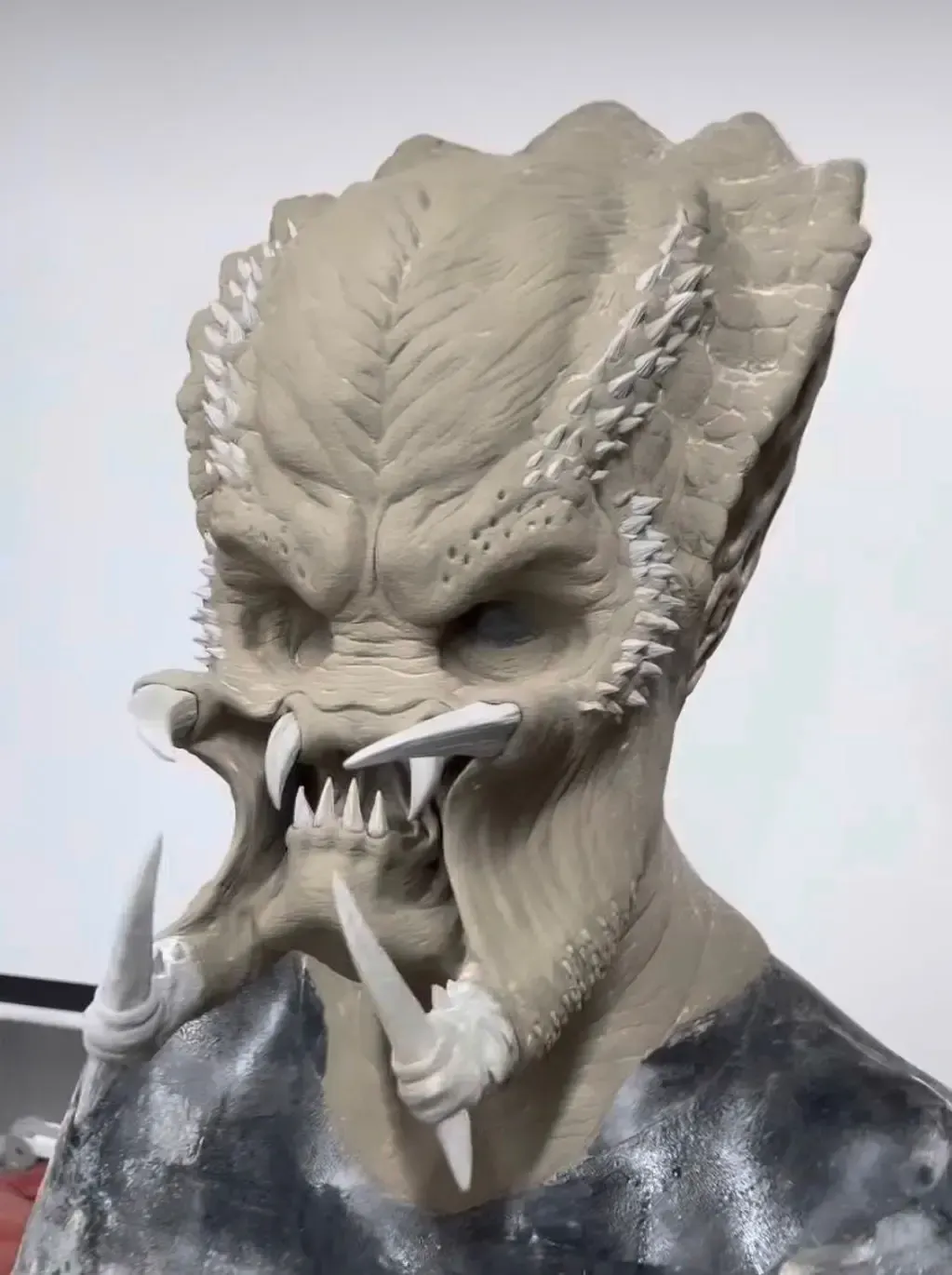 A detailed, unpainted clay sculpture of a Predator creature head with textured skin, sharp fangs, and mandibles.