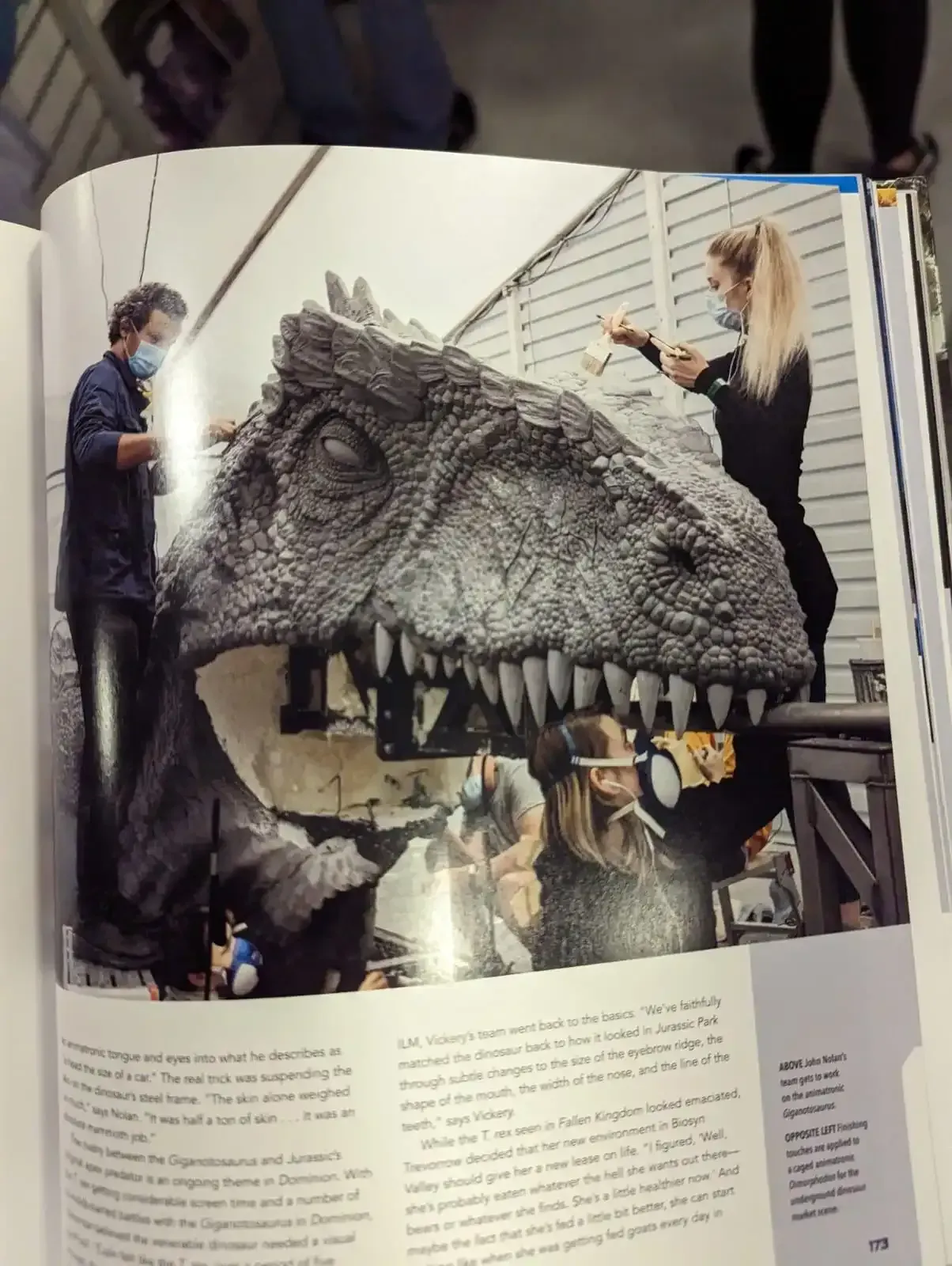 People working on the head of a dinosaur prop. Gray, realistic, indoors with lights.