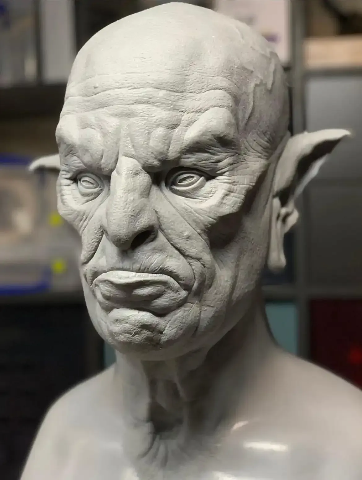 A gray, sculpted bust of a fantasy creature with pointed ears, deep wrinkles, and a somber, humanoid expression.