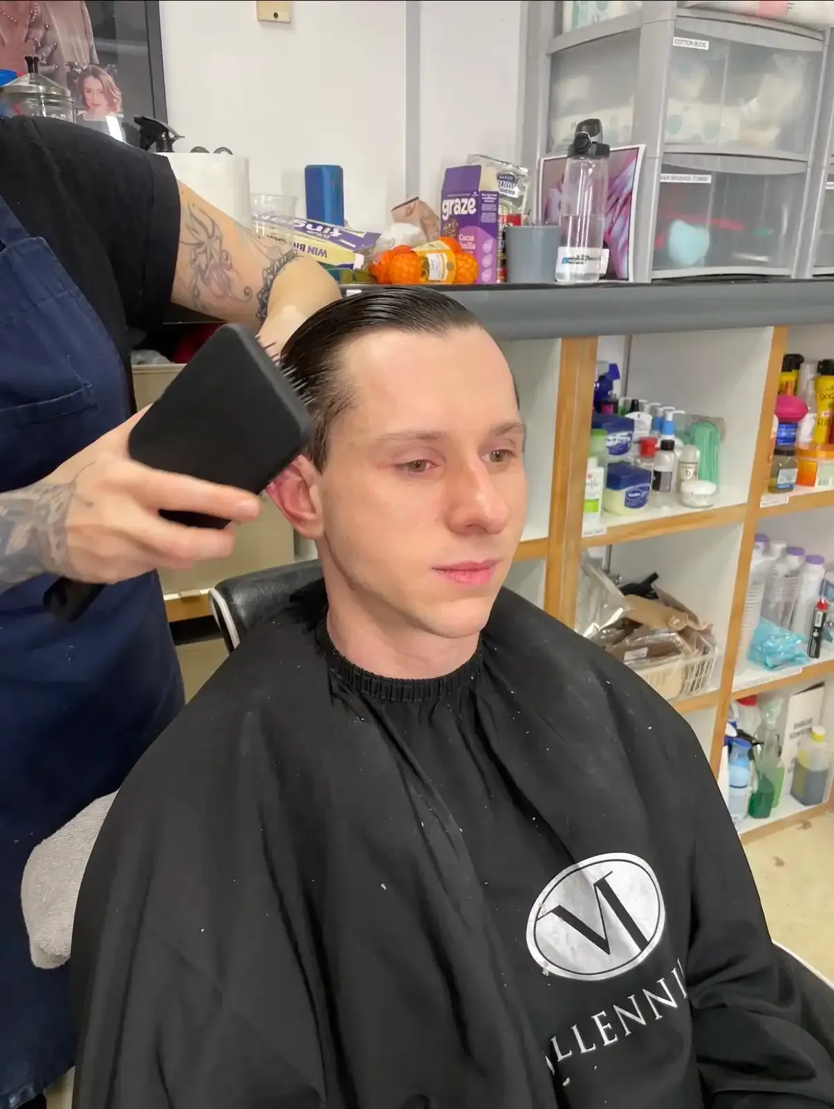 Person getting a haircut; stylist holding a hair-cutting tool. Indoor setting with beauty products.
