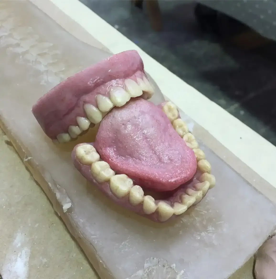 A dental model showing upper and lower dentures with a pink tongue, positioned on a translucent molding tray.