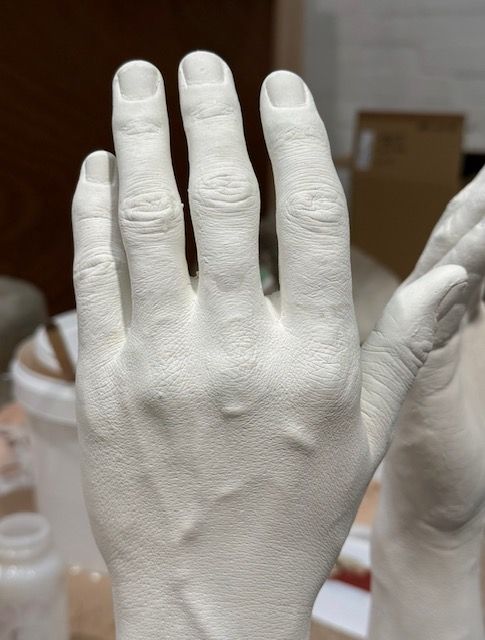 A white, detailed plaster cast of a human hand, captured from the back, showing visible knuckles and veins.