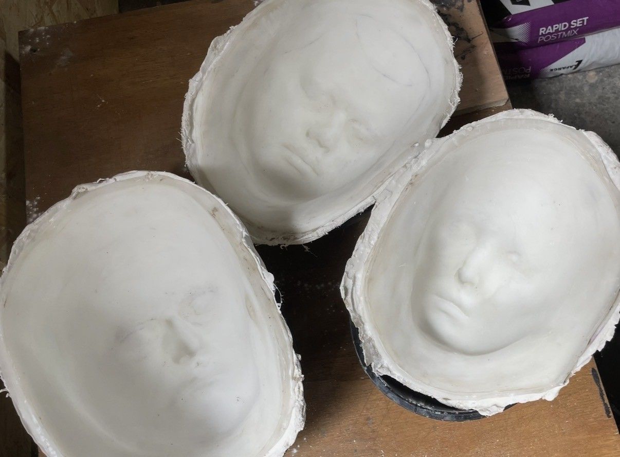 Three white plaster face masks resting on a wooden surface.