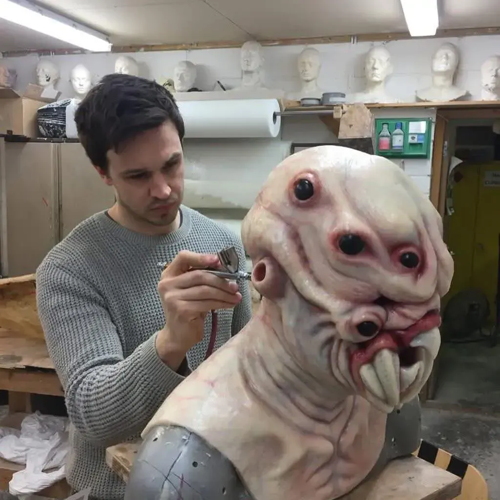 Artist sculpting a clay portrait bust at a workbench in a studio with reference photos behind her