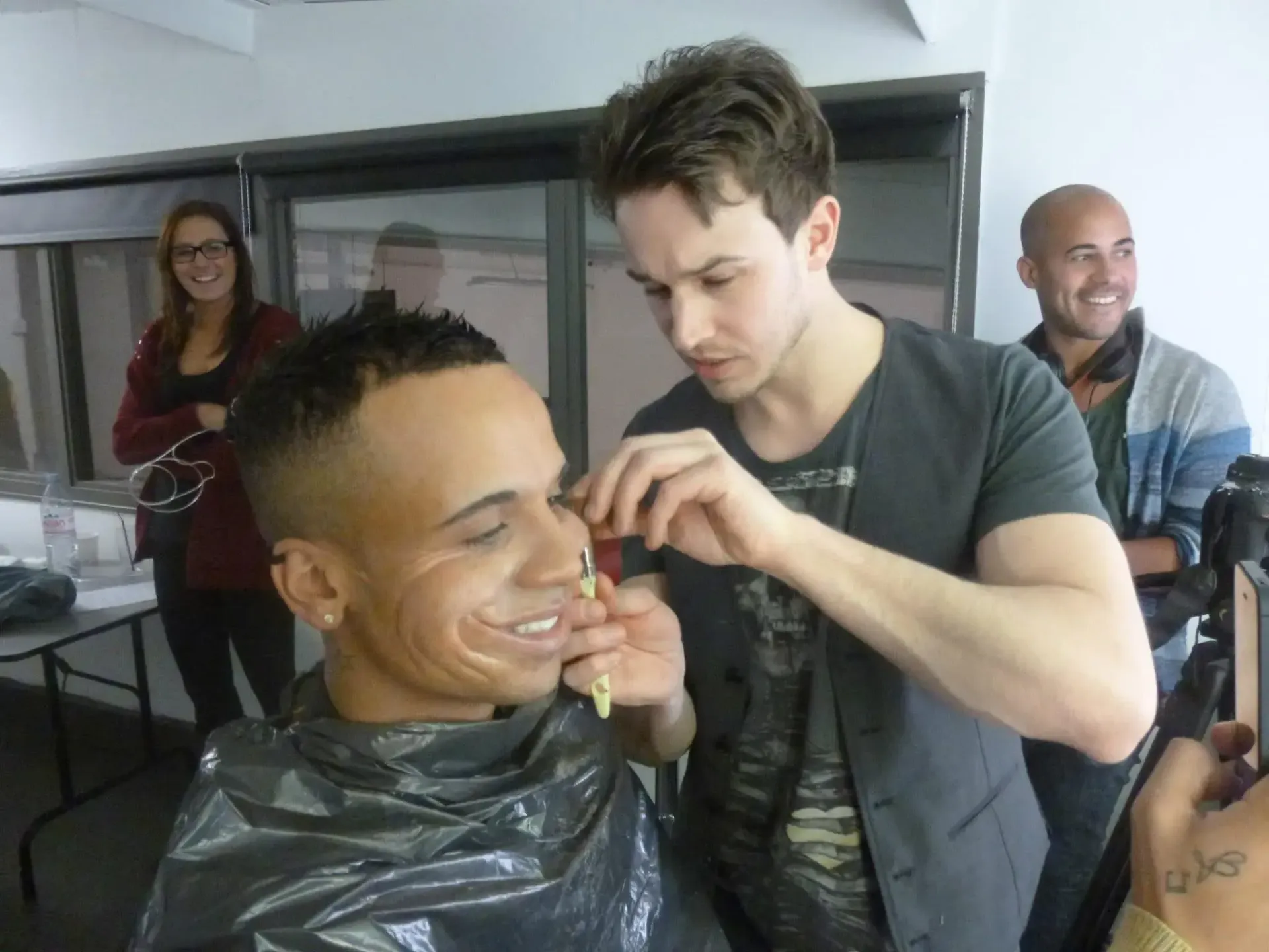 Makeup artist applying makeup to a seated man in a salon mirror station