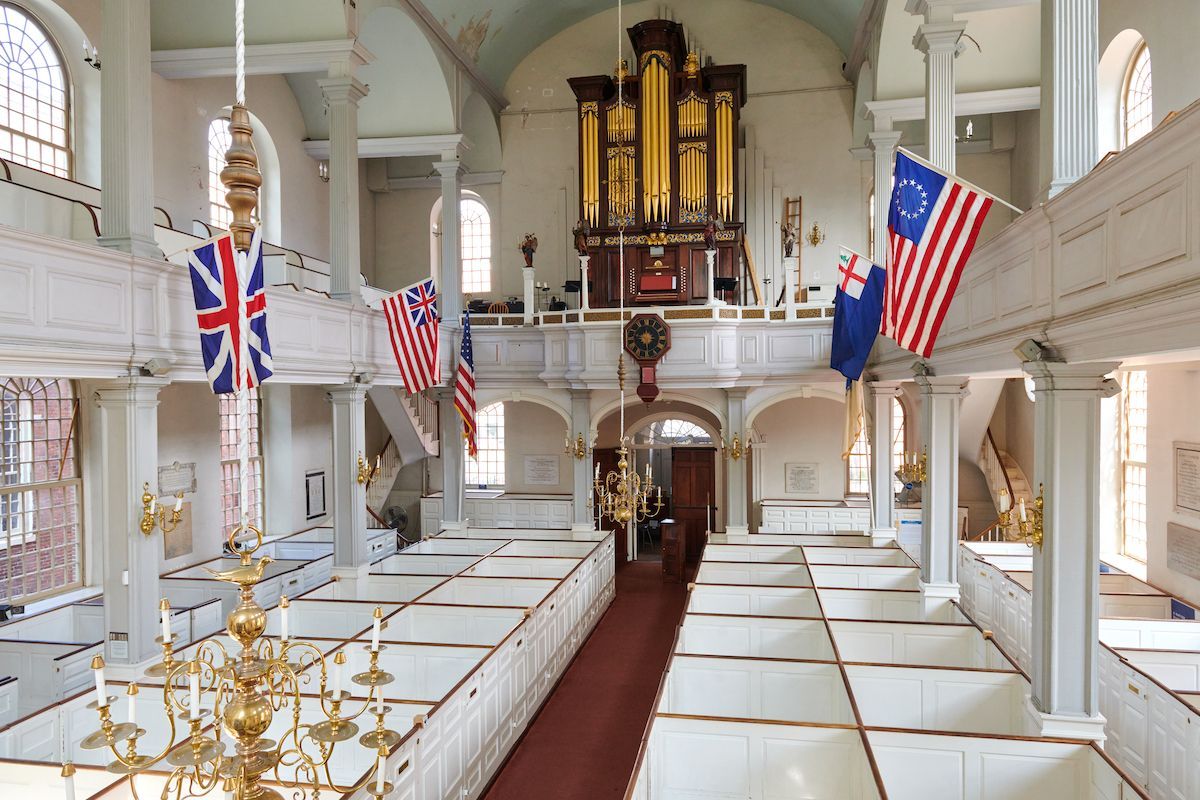 Historic church interior with Union Jack and U.S. flags, white pews, and a large pipe organ at the altar