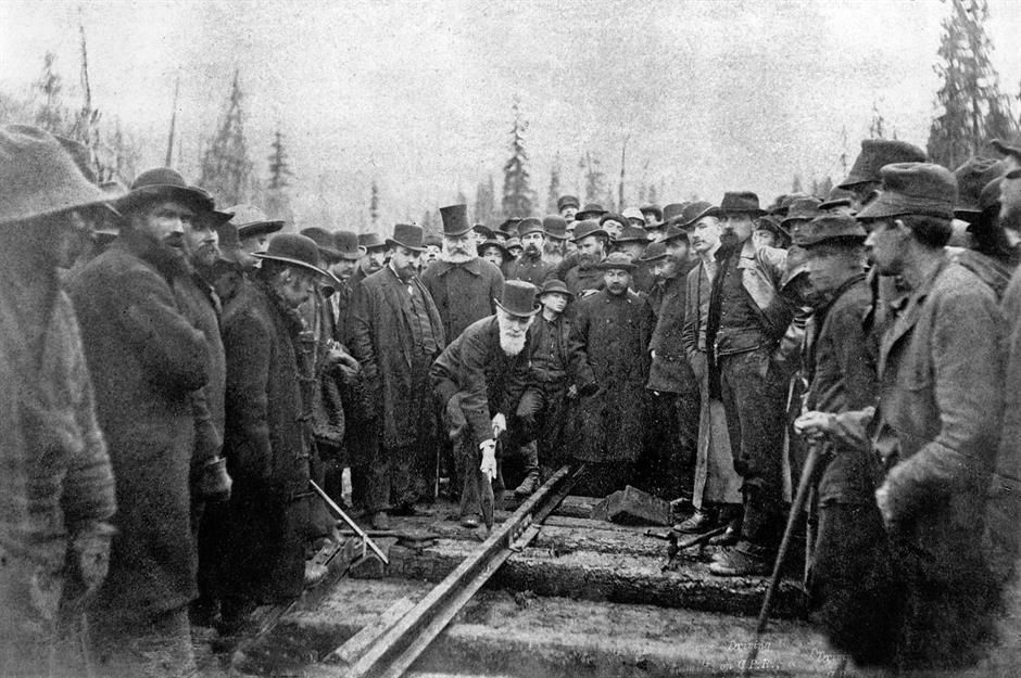 Men gathered around railroad tracks at a logging site, inspecting an engine or rail equipment.