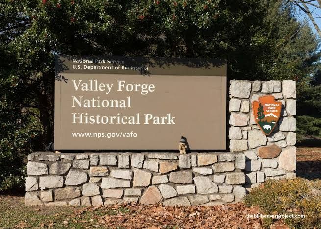 Valley Forge National Historical Park entrance sign on a stone wall with park emblem and trees behind