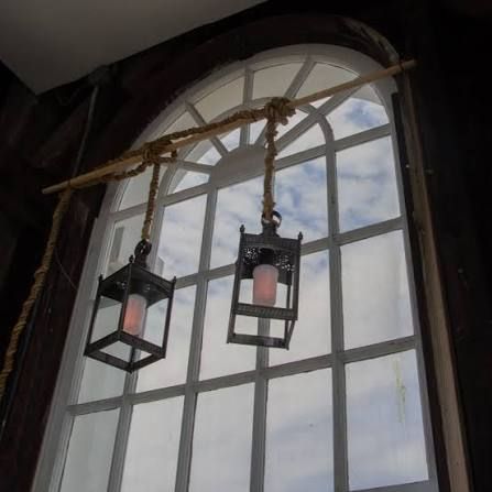 Two hanging lanterns beside a tall arched window with cloudy sky outside