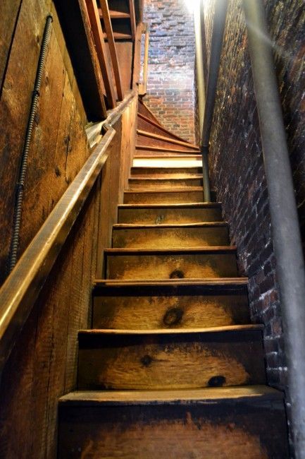 Narrow wooden staircase in a brick alley, viewed upward in warm light