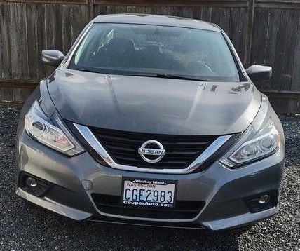 A gray nissan altima is parked in front of a wooden fence.