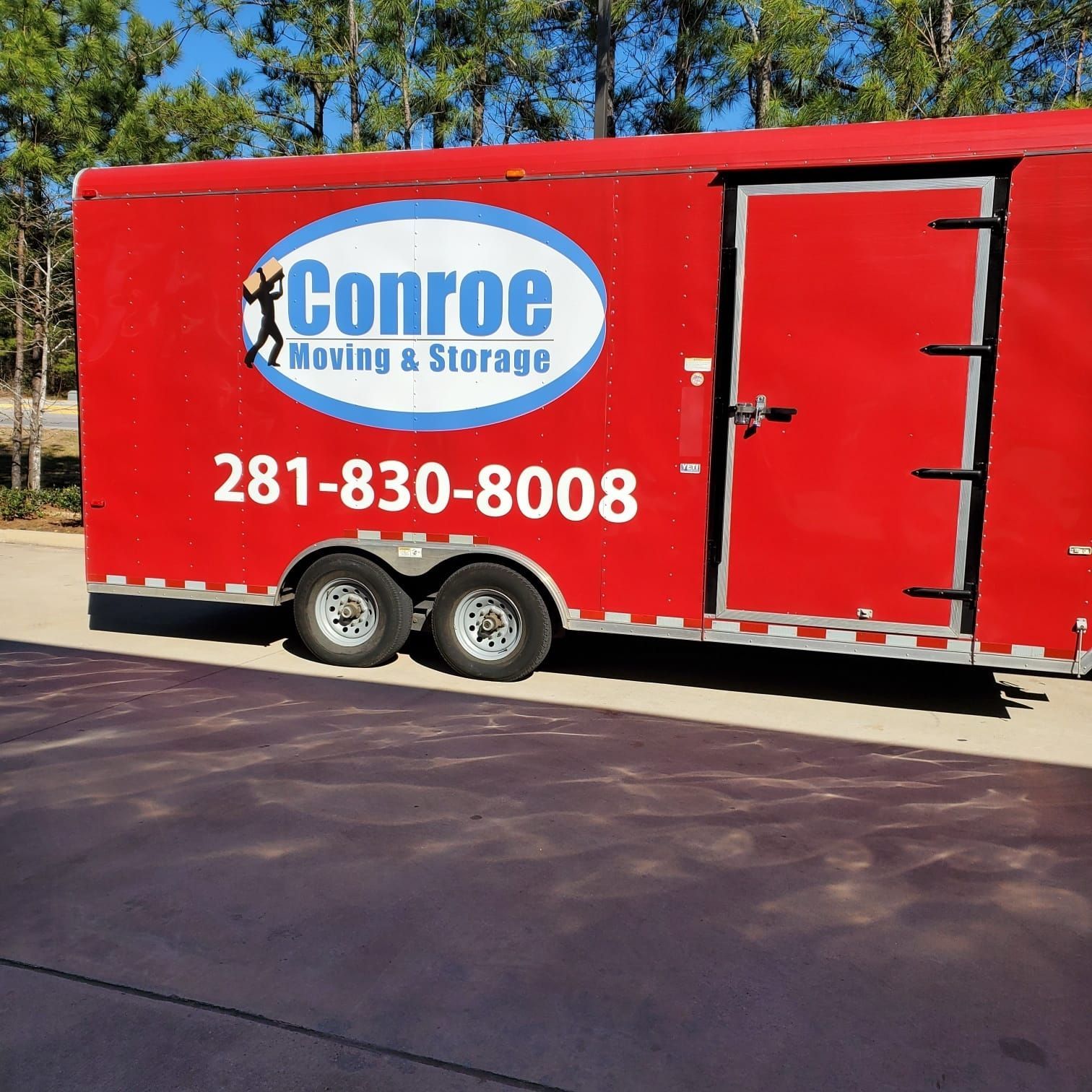 Red Conroe Moving & Storage trailer with phone number parked outdoors on pavement