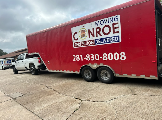 A red moving trailer is parked next to a white truck.