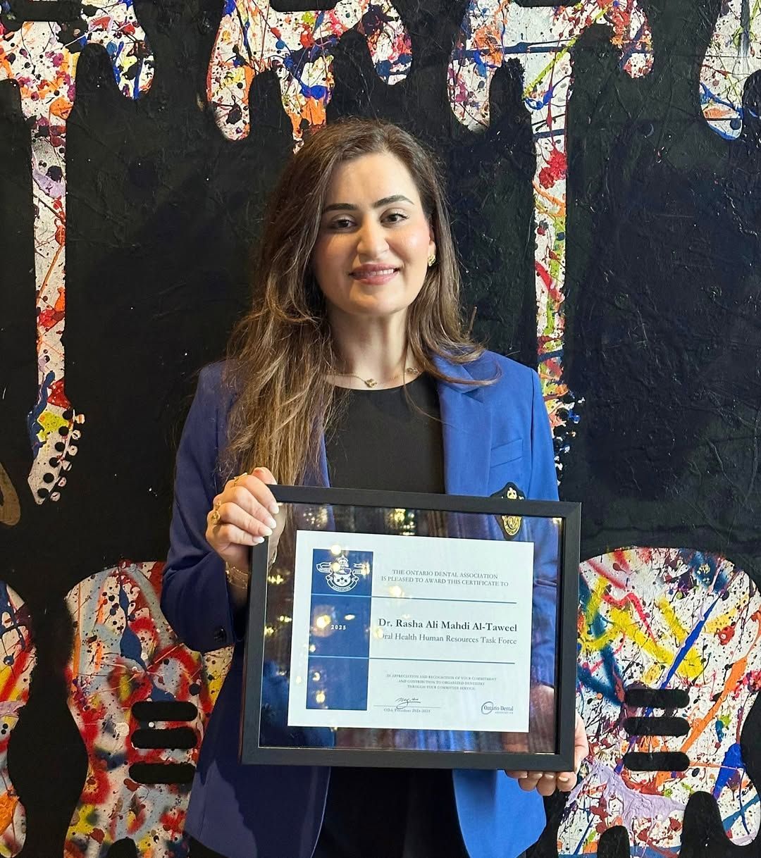 Woman in a blue blazer holding a framed certificate in front of a colorful mural
