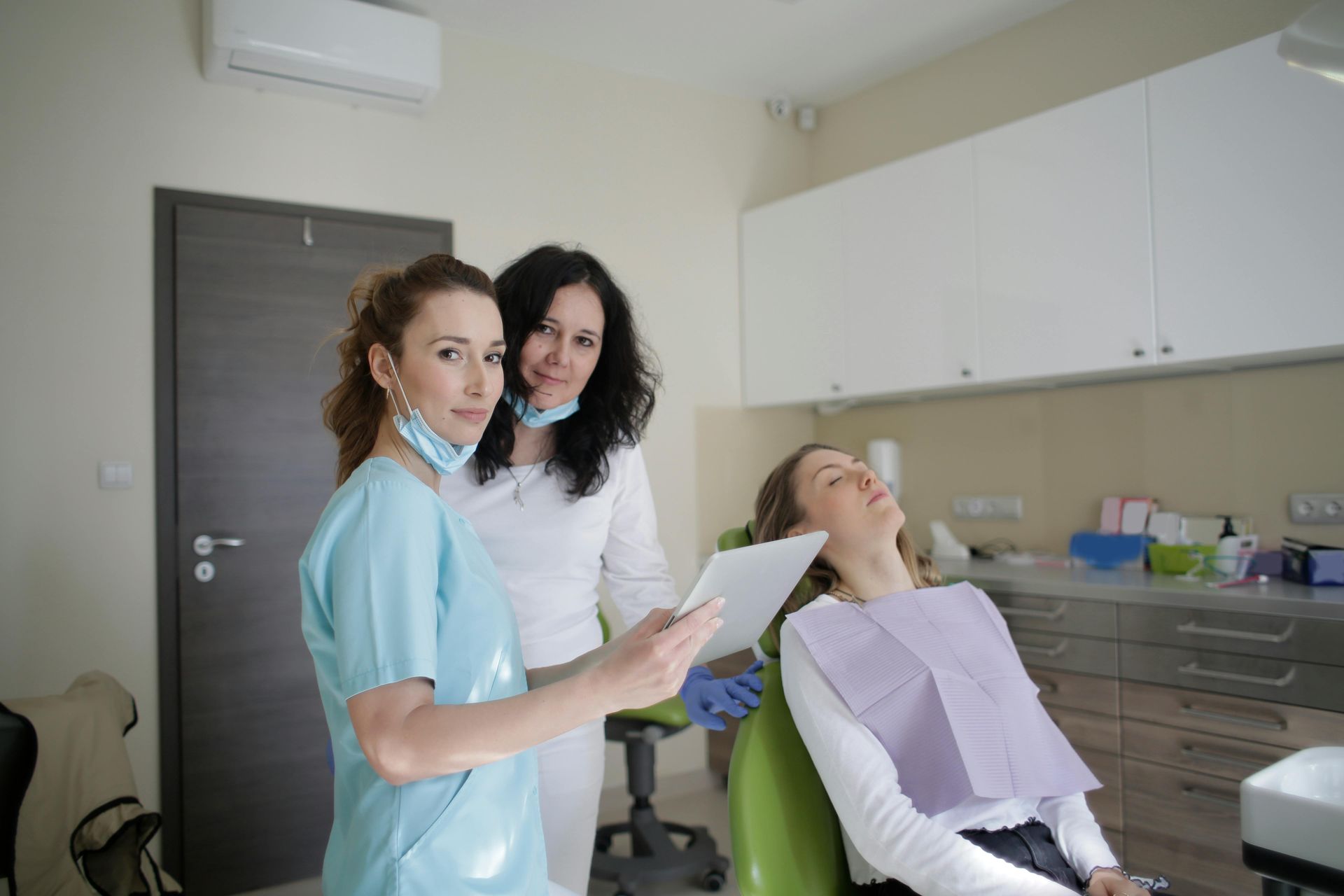 Dental clinic exam with two staff and a patient in a chair, one holding paperwork.