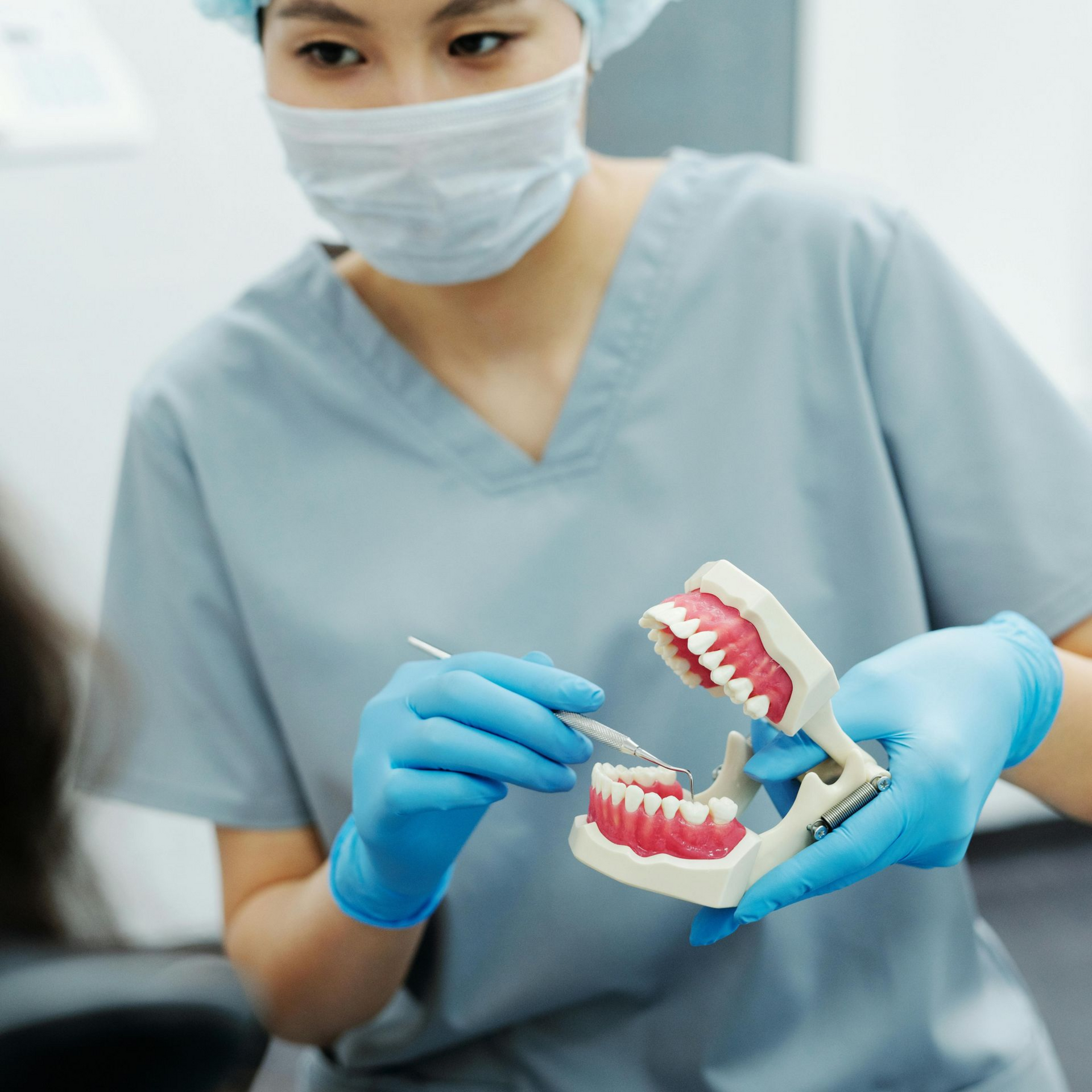 Dentist in blue scrubs and mask demonstrating a dental model with a toothbrush in a clinic