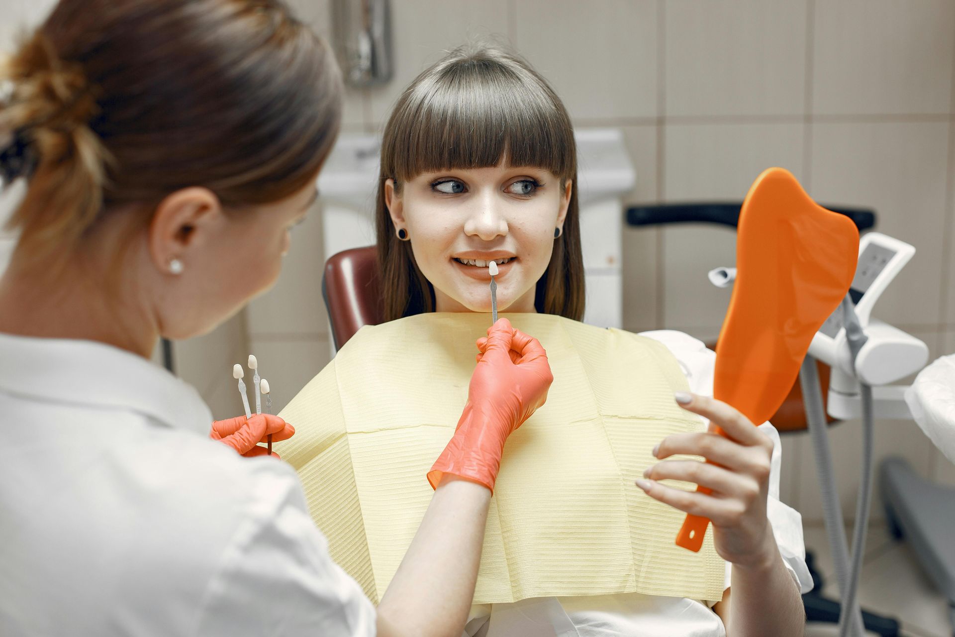 Dentist showing a patient a dental mold while wearing orange gloves in a clinic