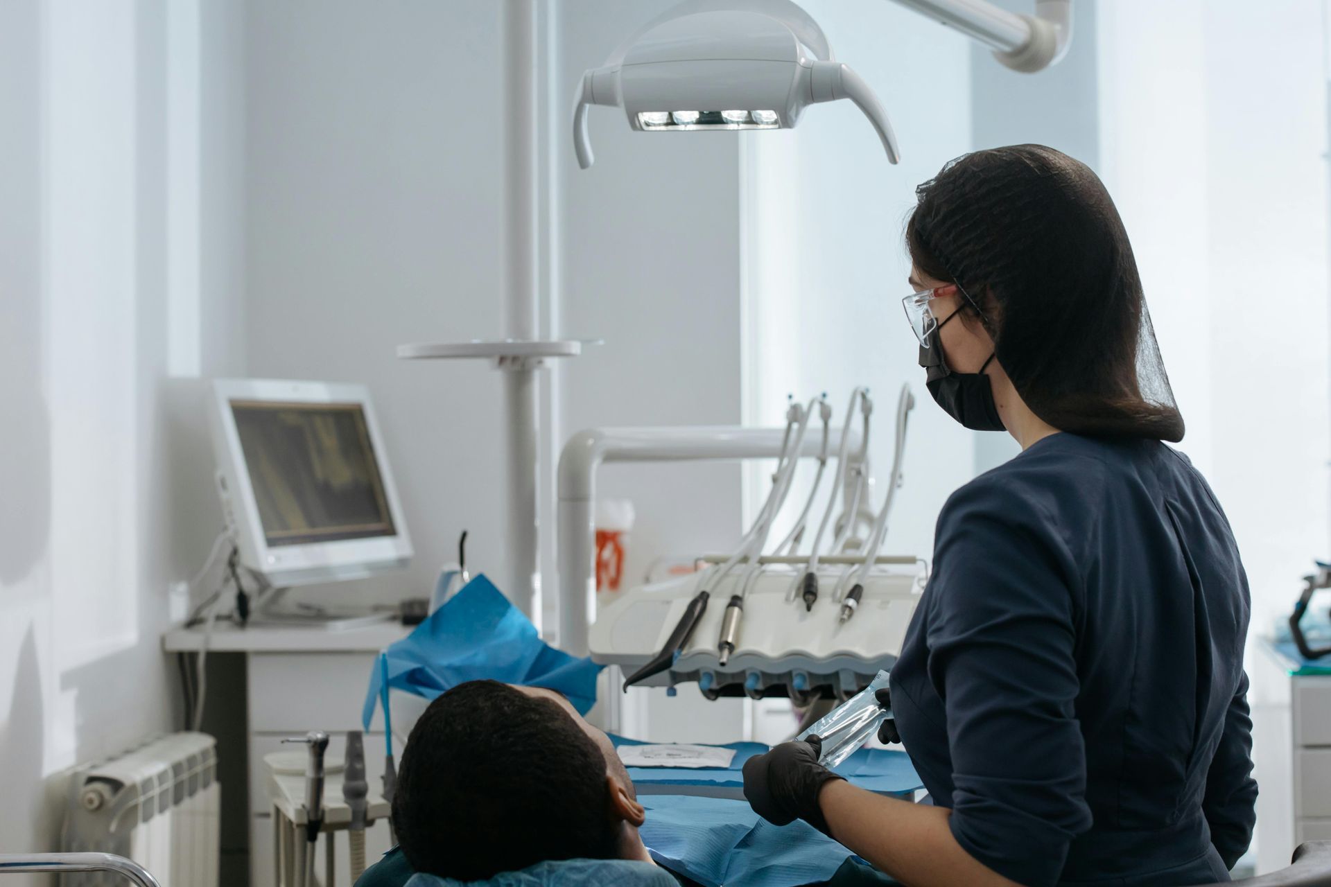 Dentist and patient in a dental clinic, with tools, chair, and overhead exam light.