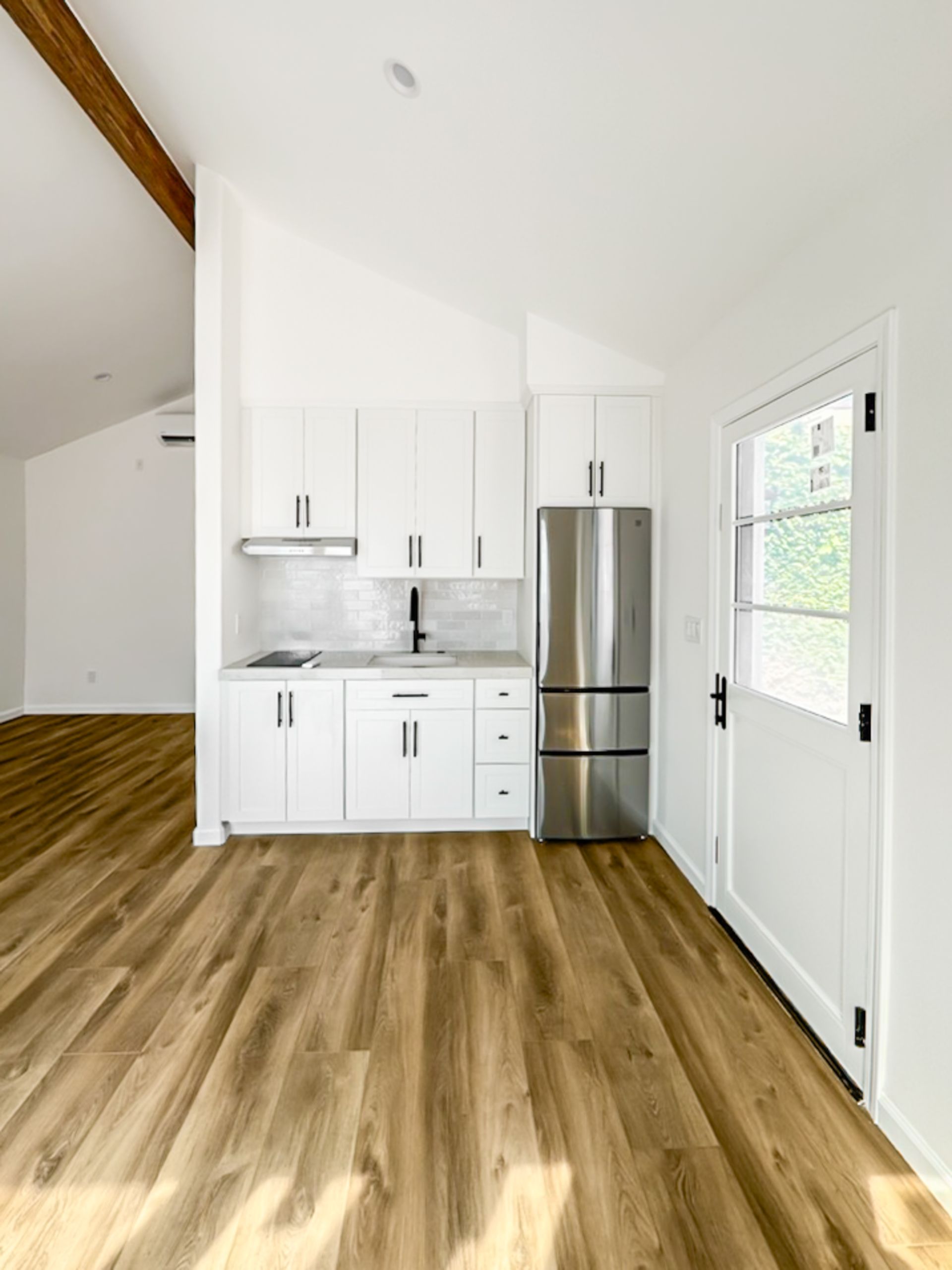 Small modern kitchen with white cabinets, stainless fridge, wood floors, and a white door with window.