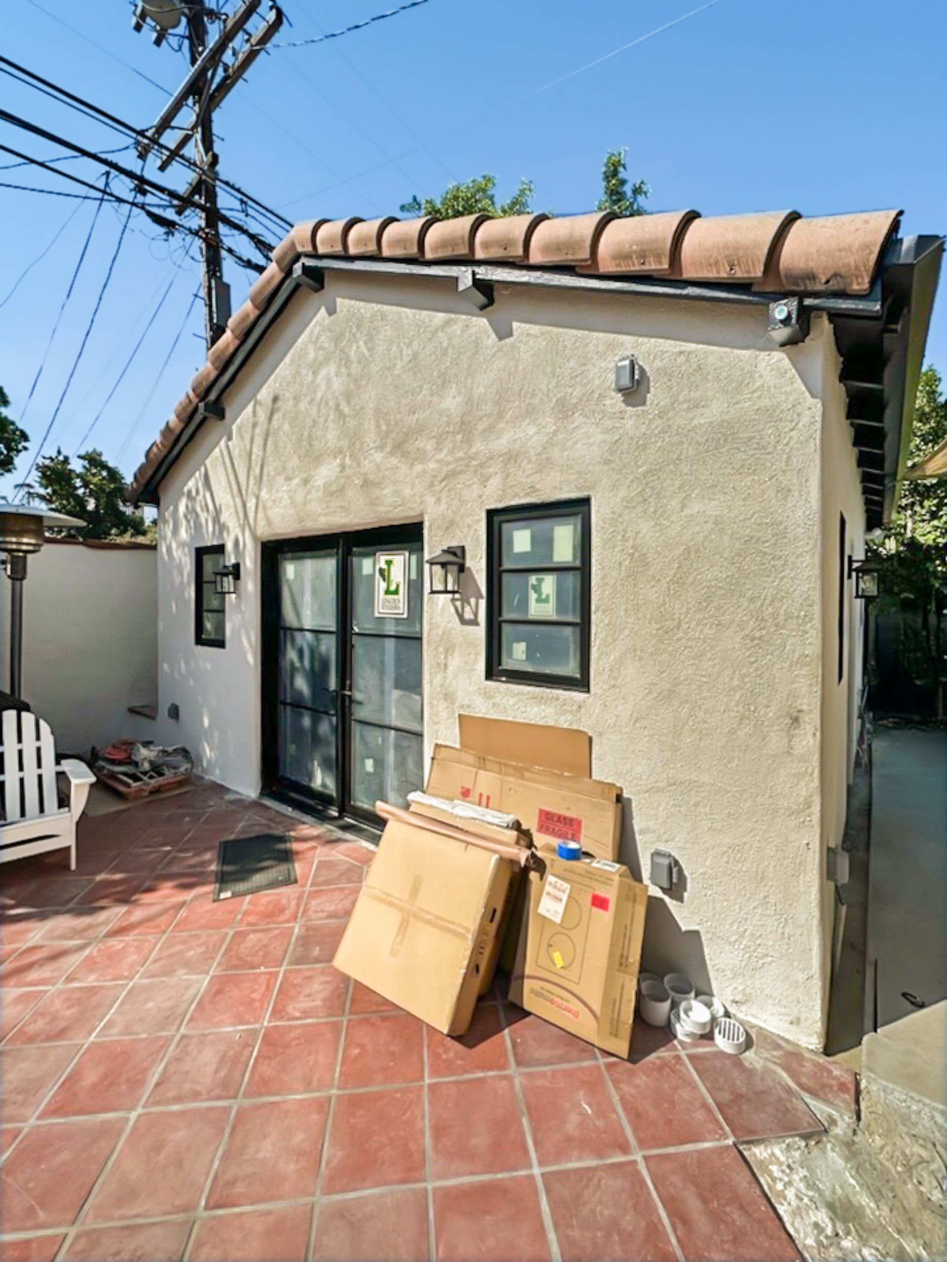 Small stucco building with tiled roof, glass door, window, and boxes on a red-tiled patio.