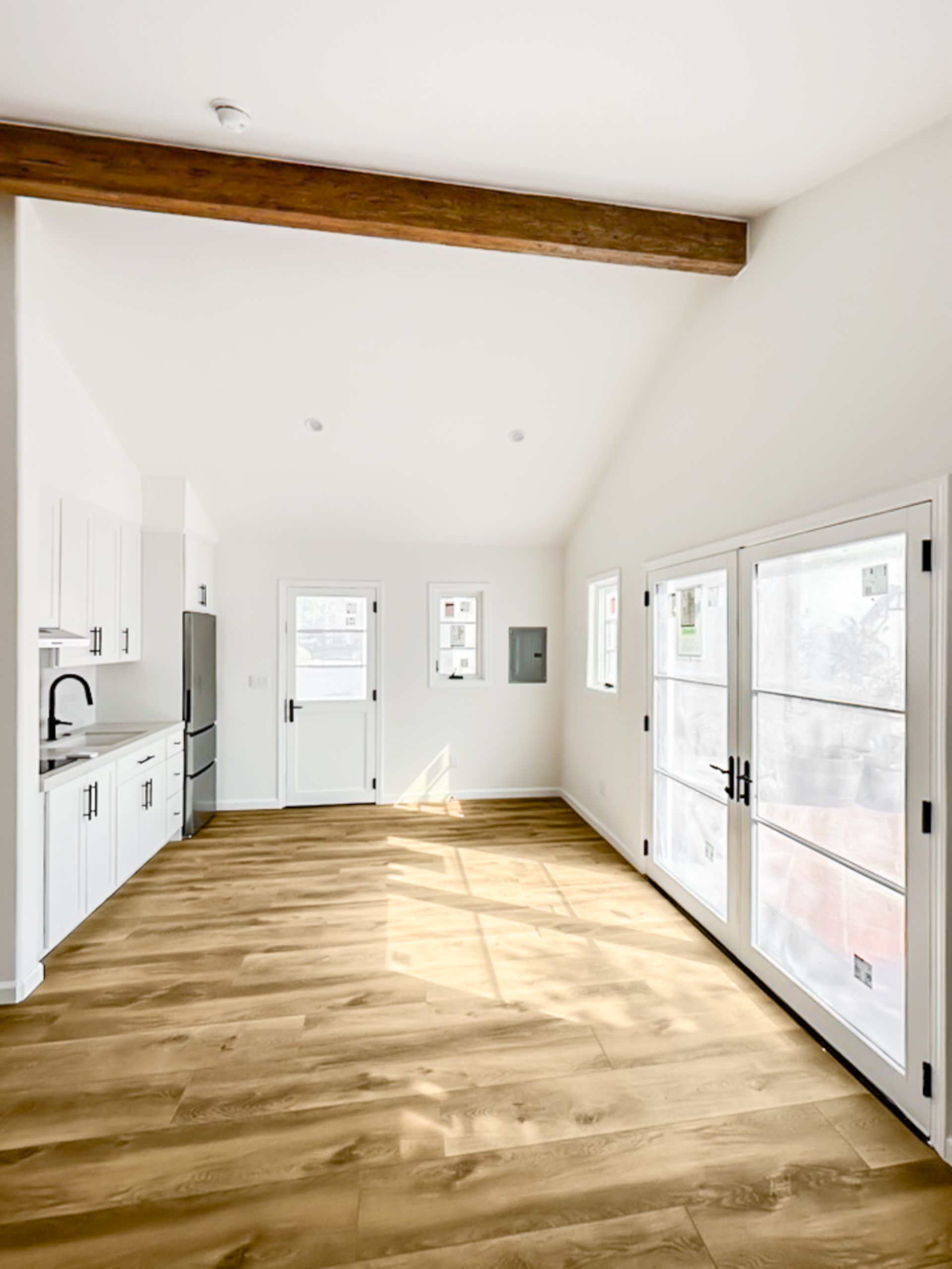 Bright empty kitchen with white walls, wood floor, exposed beam, and French doors to the outside