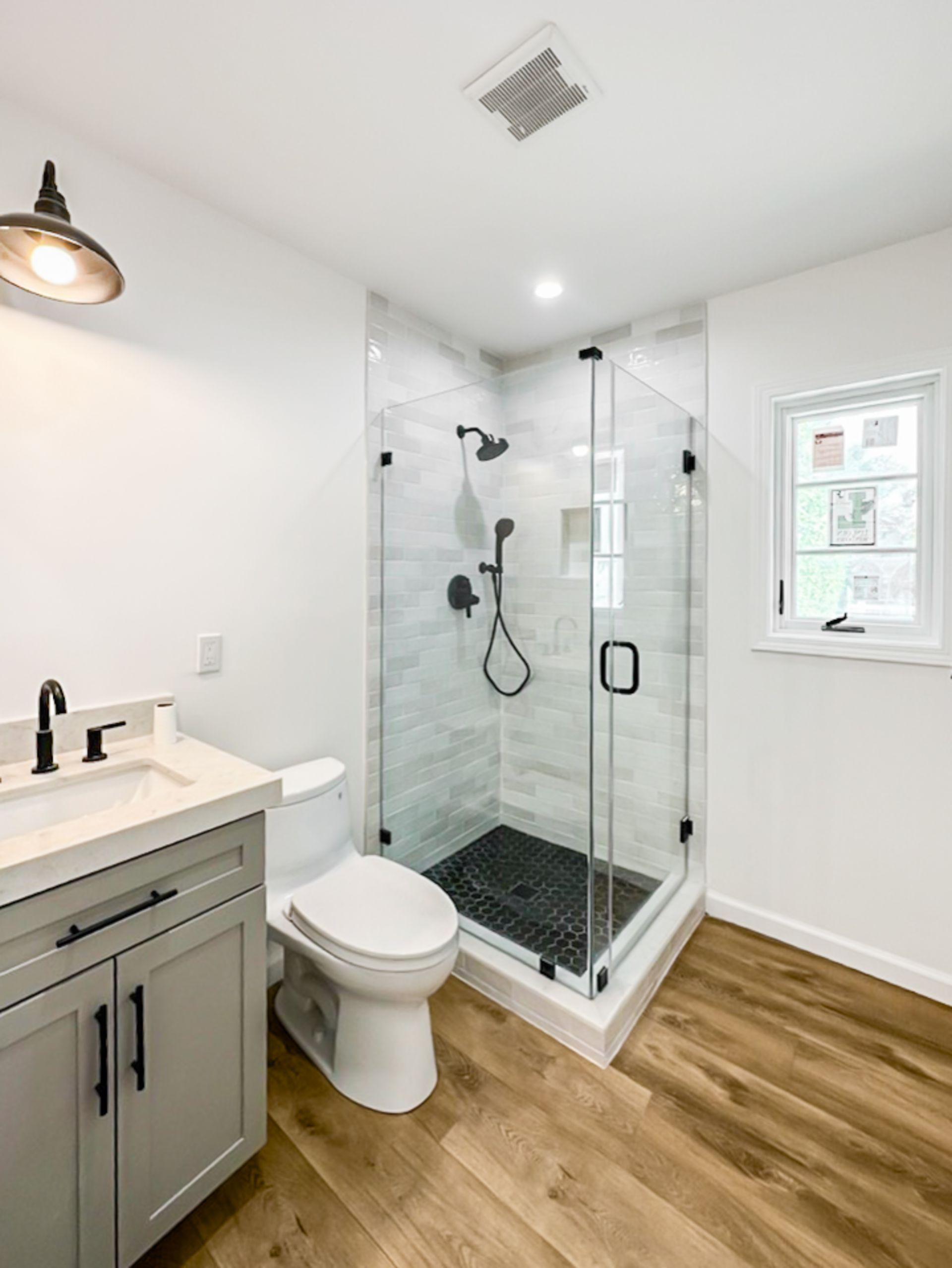 Modern bathroom with glass shower, gray vanity, white toilet, and wood-look floor