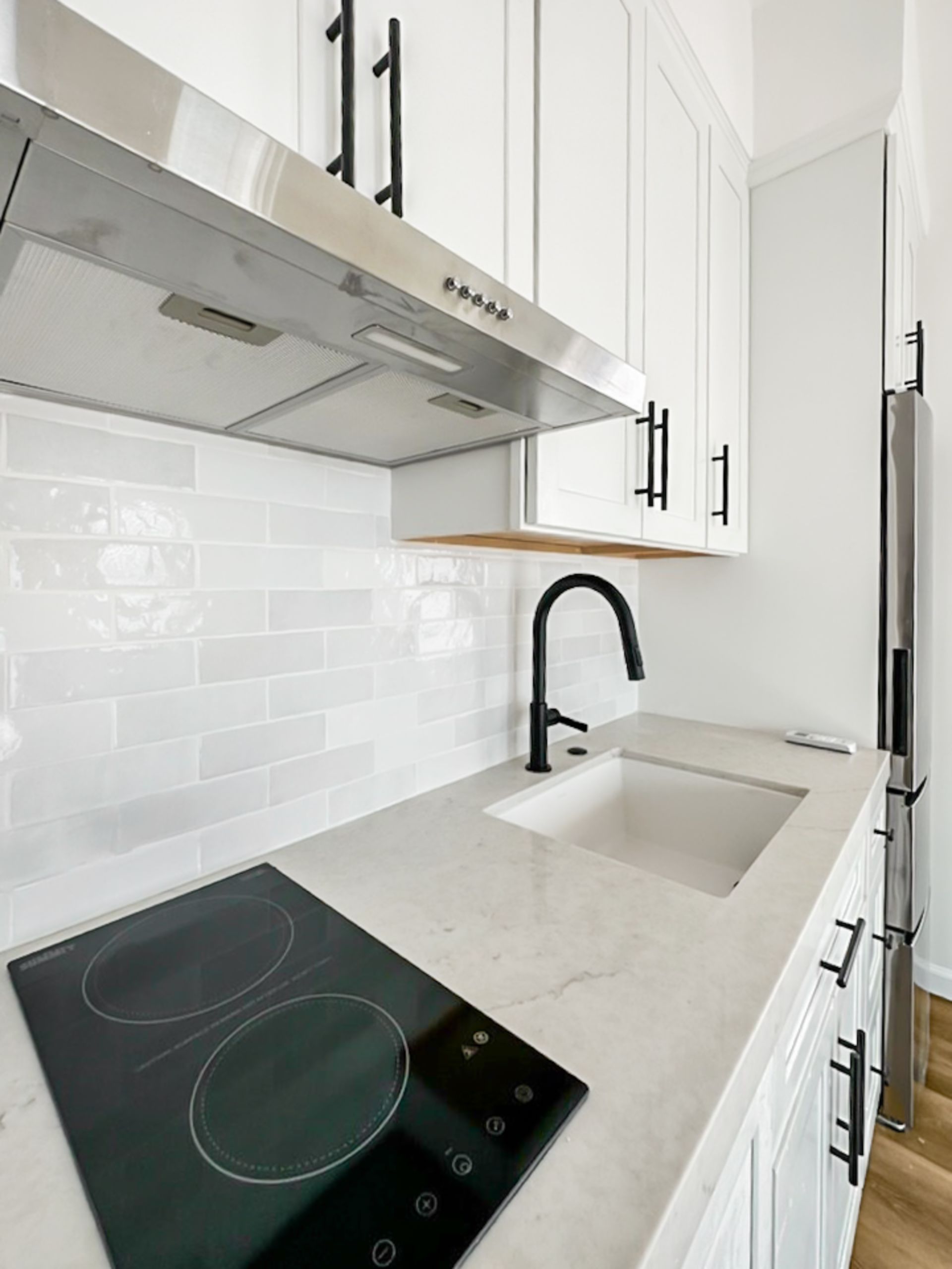 Modern white kitchen with black stovetop, sink, and stainless range hood