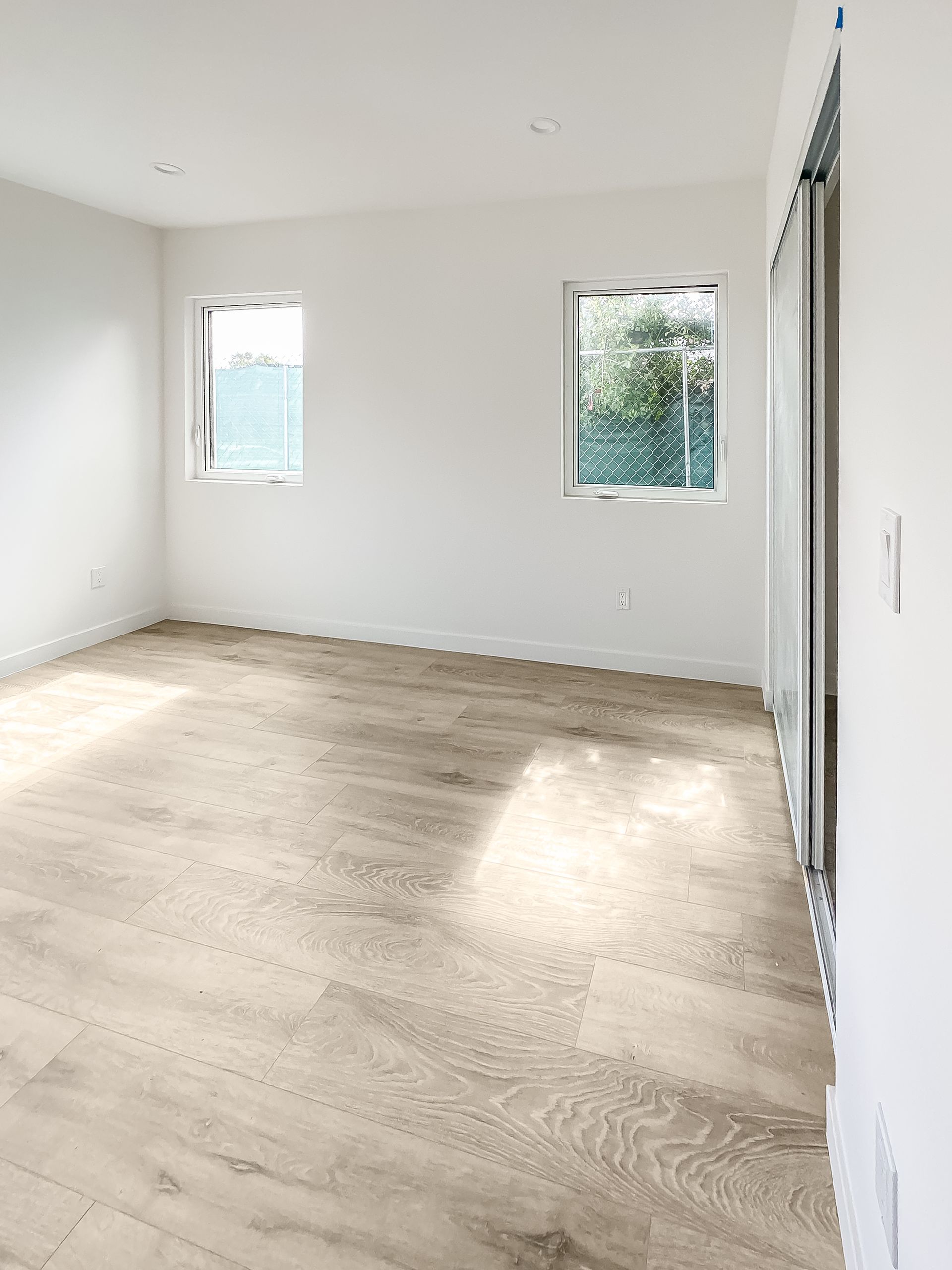 Empty bright room with light wood floor, white walls, and two small windows.
