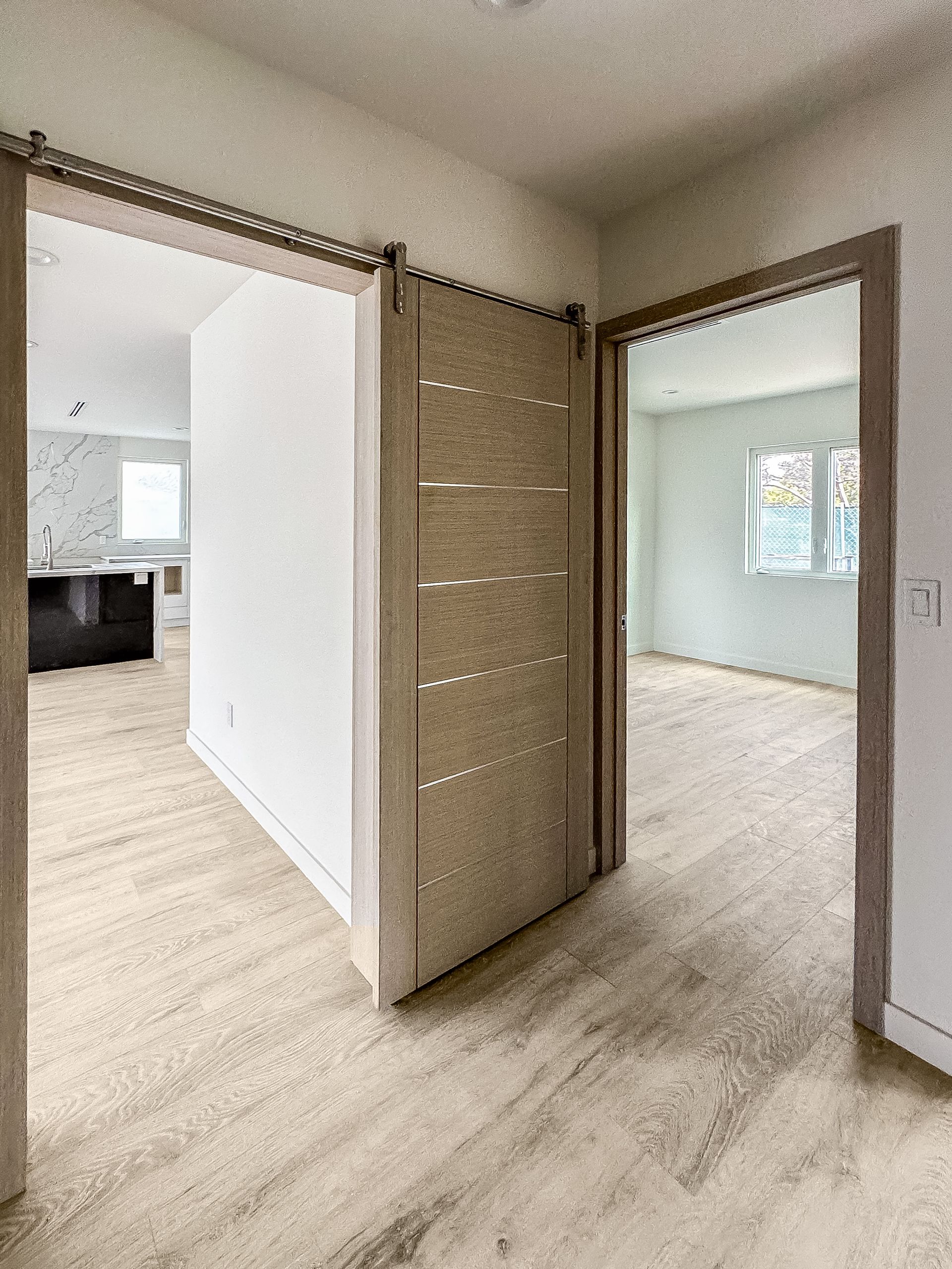Empty hallway with open doorways, light wood flooring, and bright rooms beyond