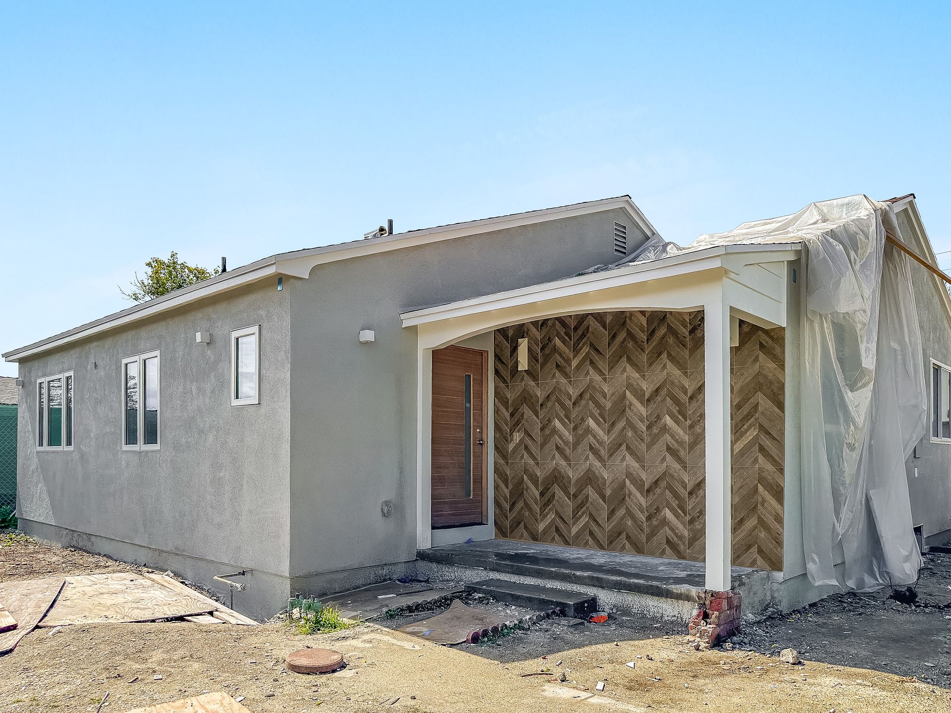 Gray single-story house under construction with covered front porch and plastic sheeting on the right side.