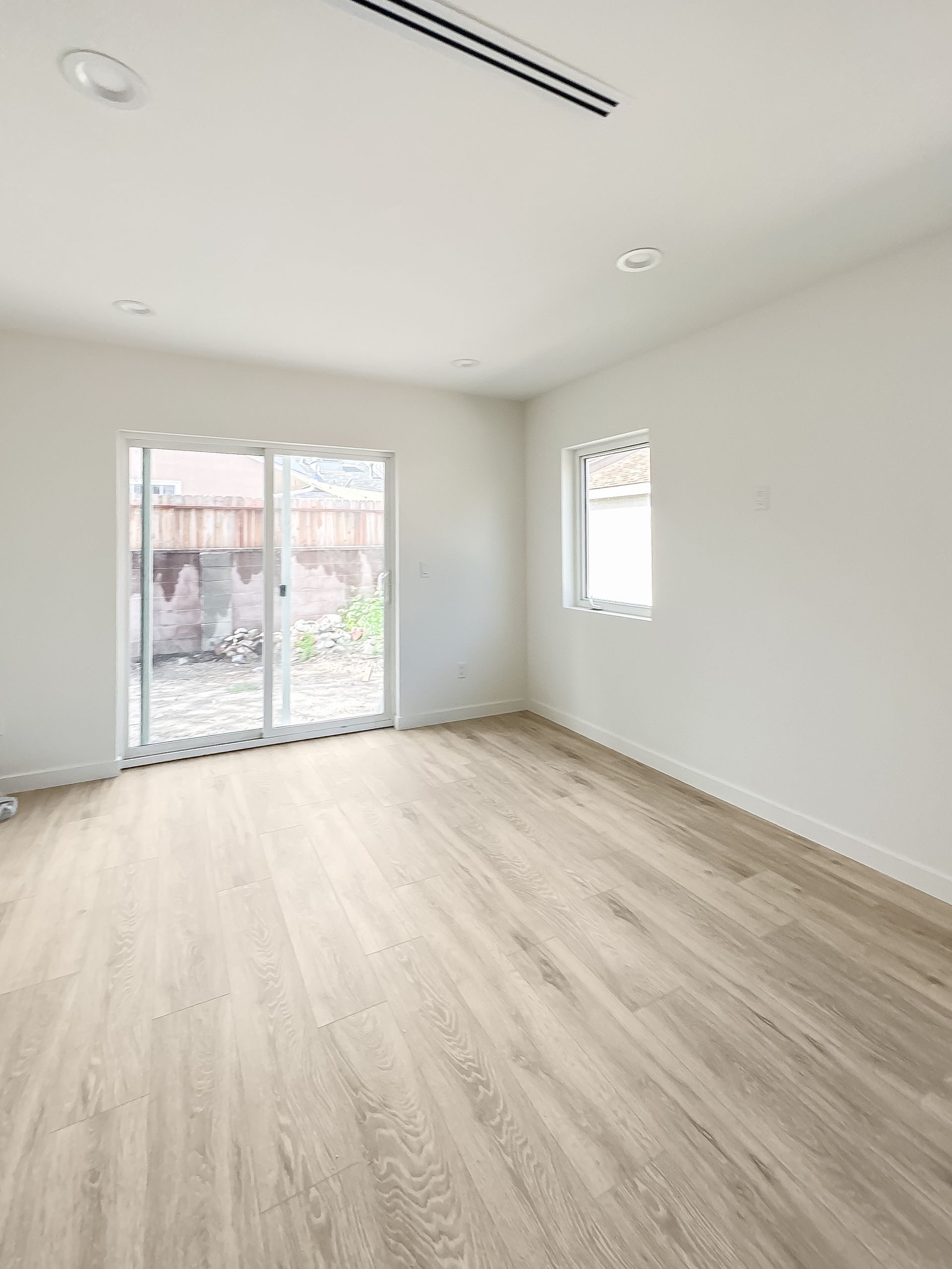 Empty bright room with light wood floors, white walls, and sliding glass doors to a patio.
