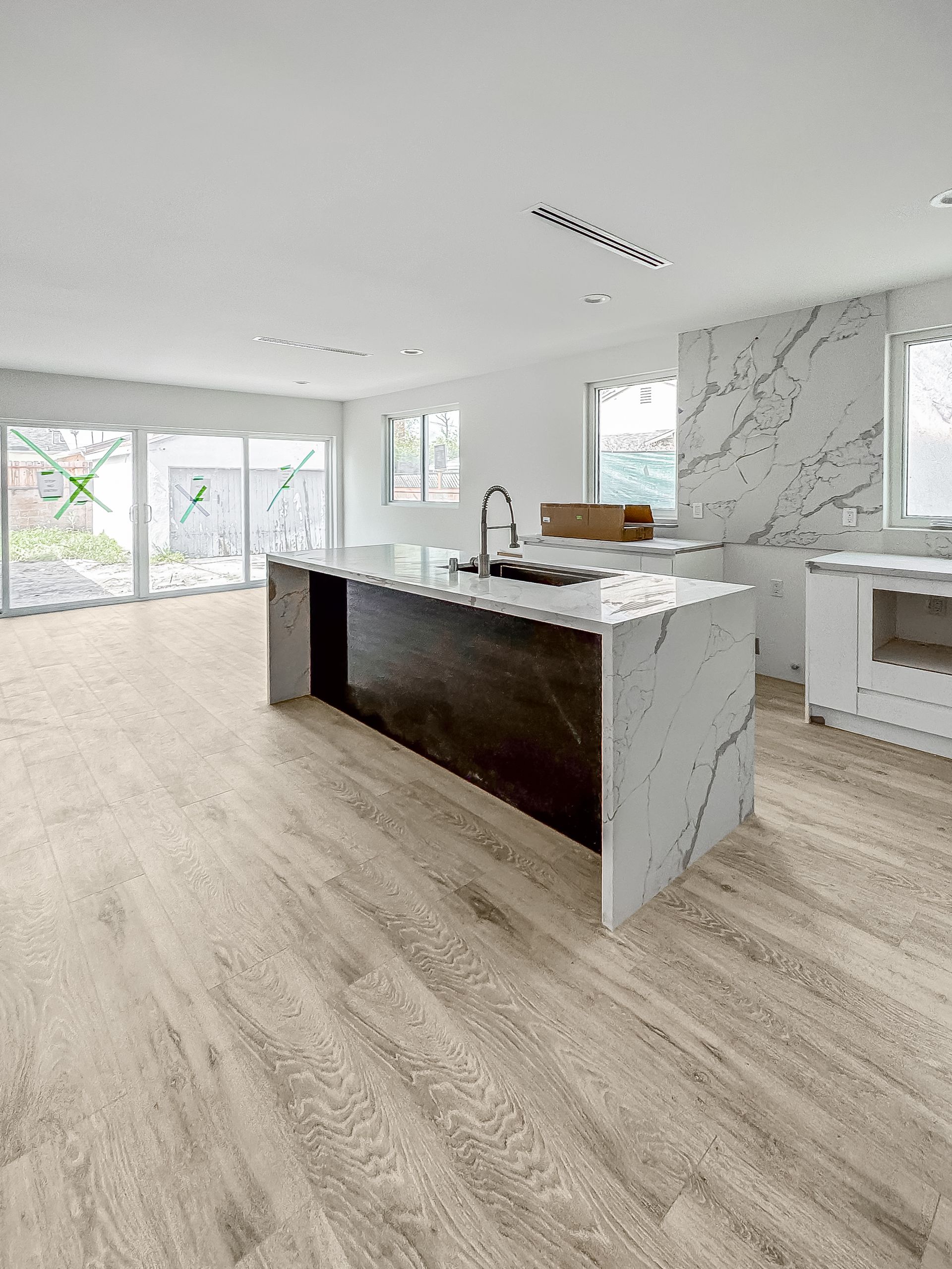 Bright modern kitchen with white marble island, dark cabinets, and large windows overlooking greenery