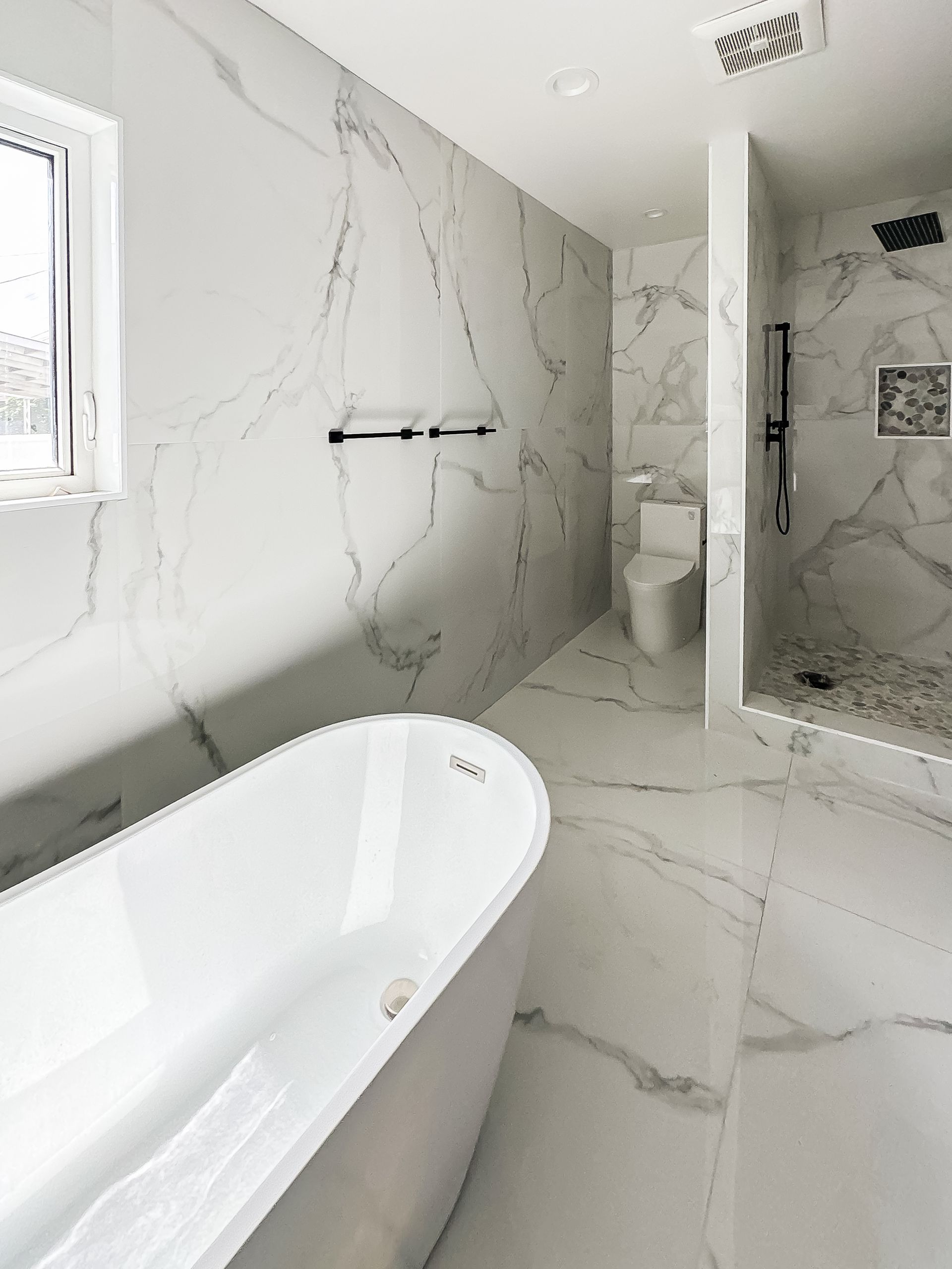 Modern white bathroom with a freestanding tub, marble-look walls, and a walk-in shower