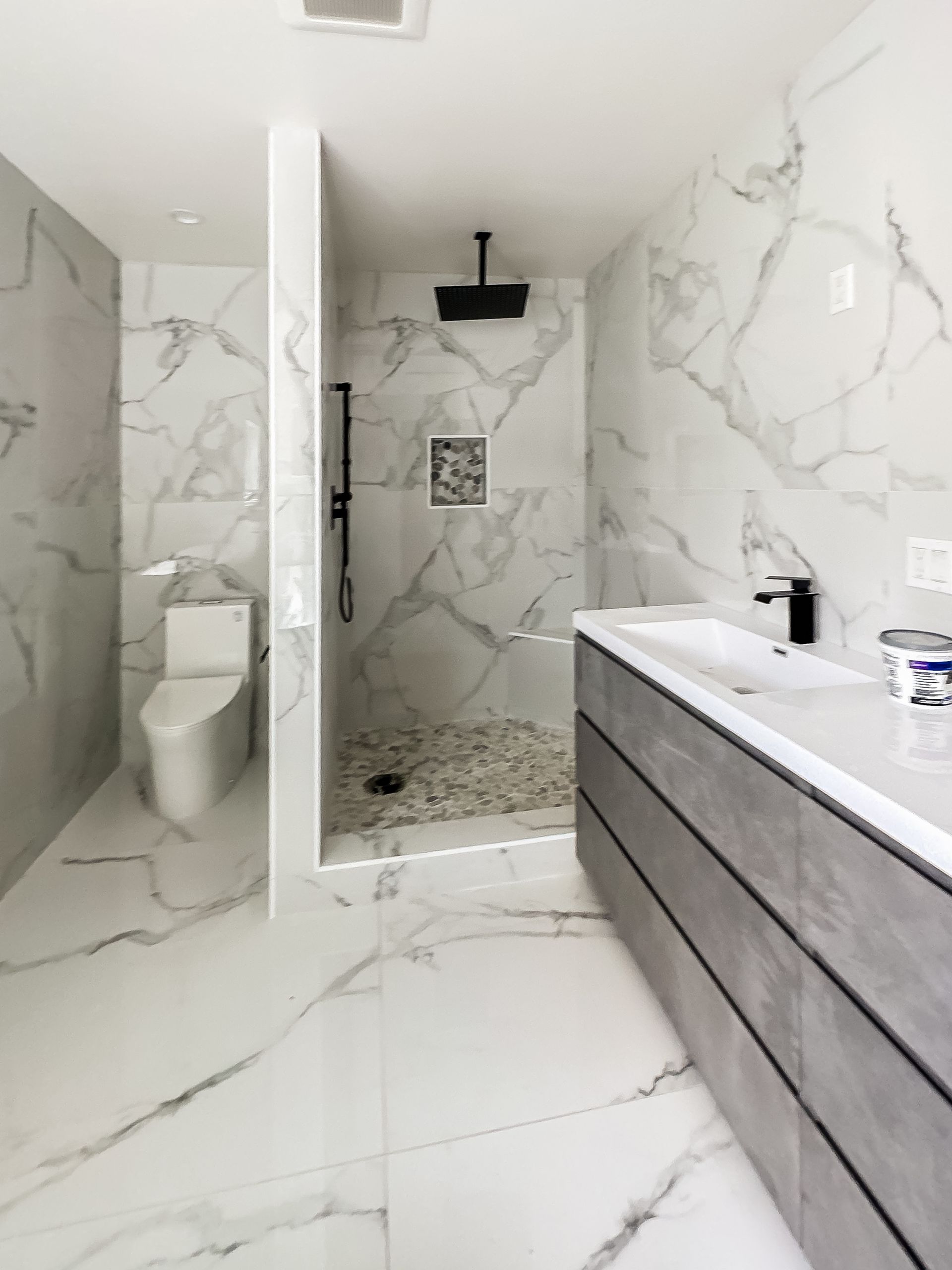 Modern marble bathroom with walk-in shower, toilet, and floating vanity