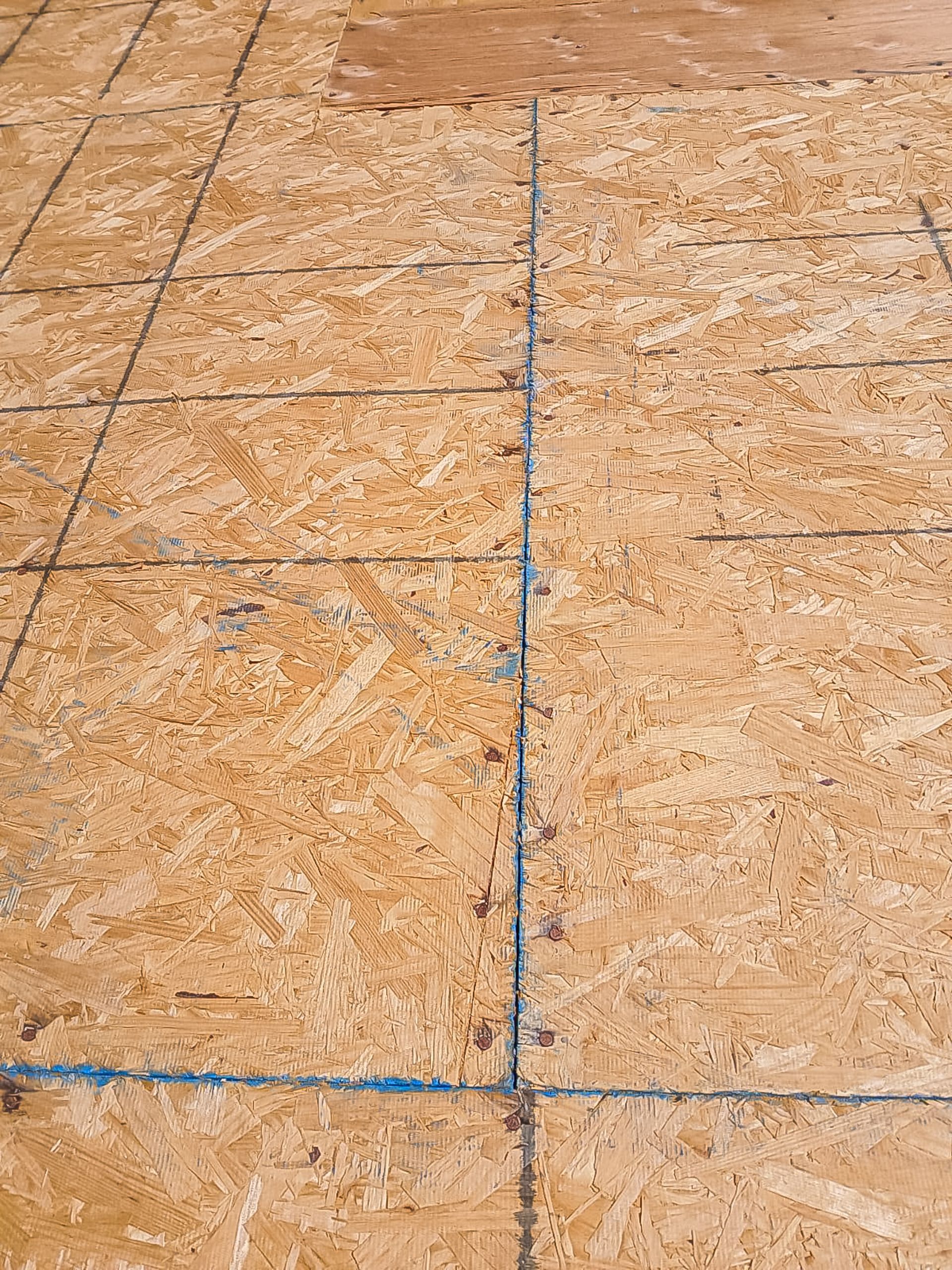 Close-up of plywood flooring with blue chalk lines marking seams and intersections